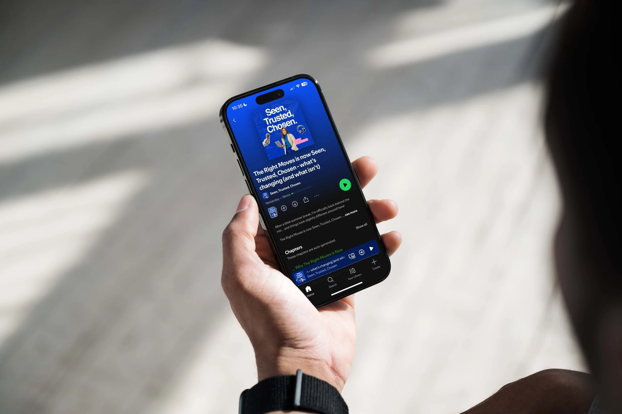 Close-up of a person holding a smartphone displaying a podcast or audiobook app with the title "Seen, Trusted, Chosen" and a woman on the cover wearing a blazer. The background of the app is blue with white text.