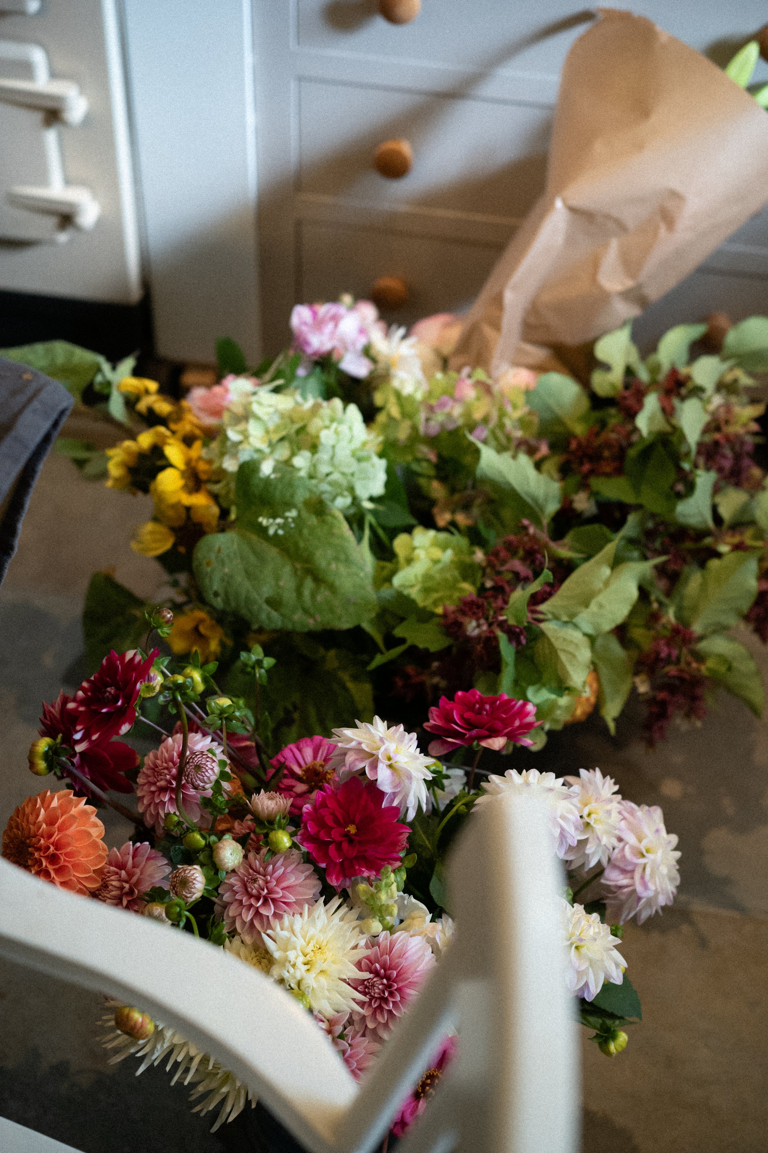 Un bouquet de fleurs colorées sur une table, avec un papier brun en arrière-plan, dans une pièce intérieure.