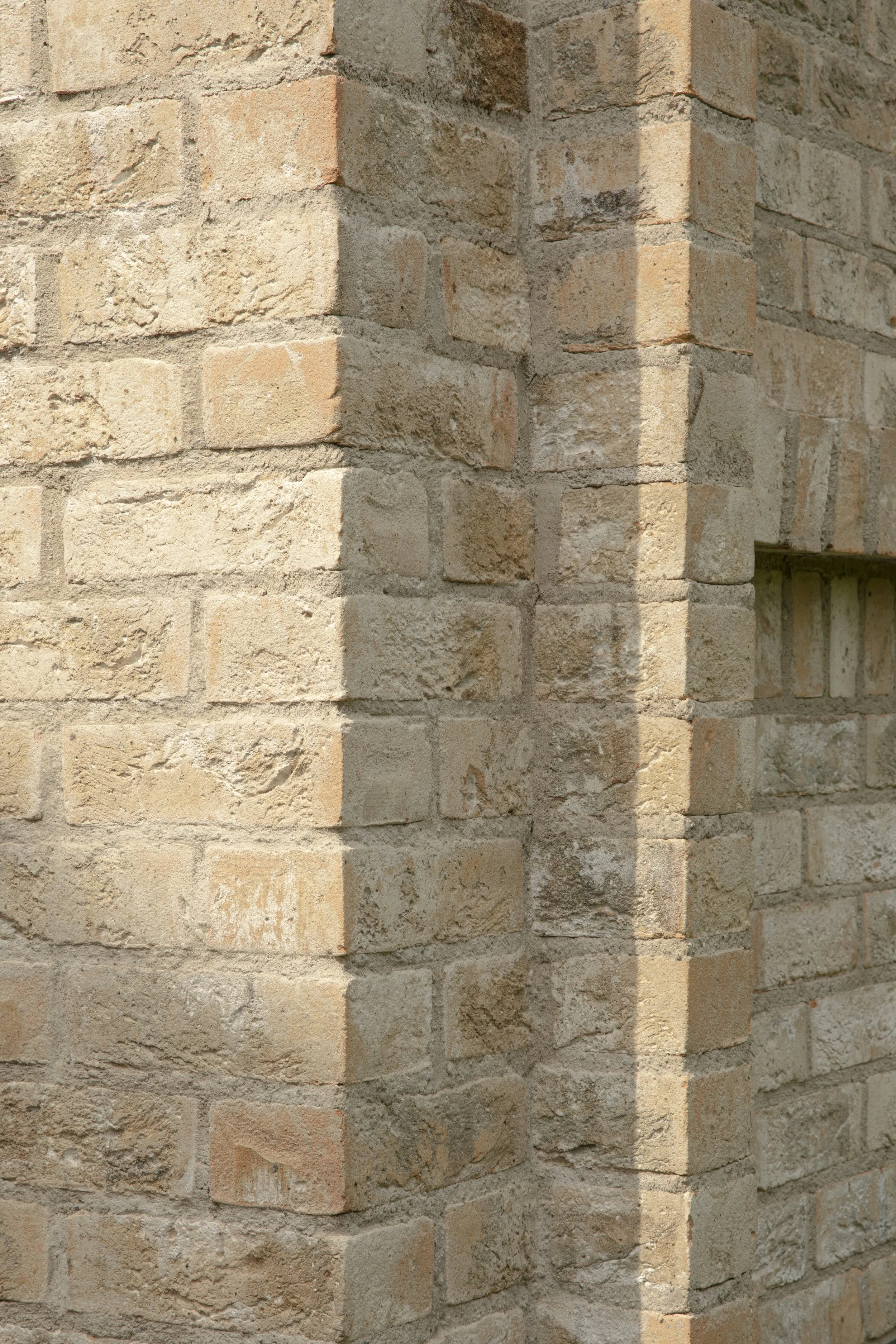 Close-up of a brick corner wall with bricks in shades of beige, tan, and light brown, showing texture and mortar details.