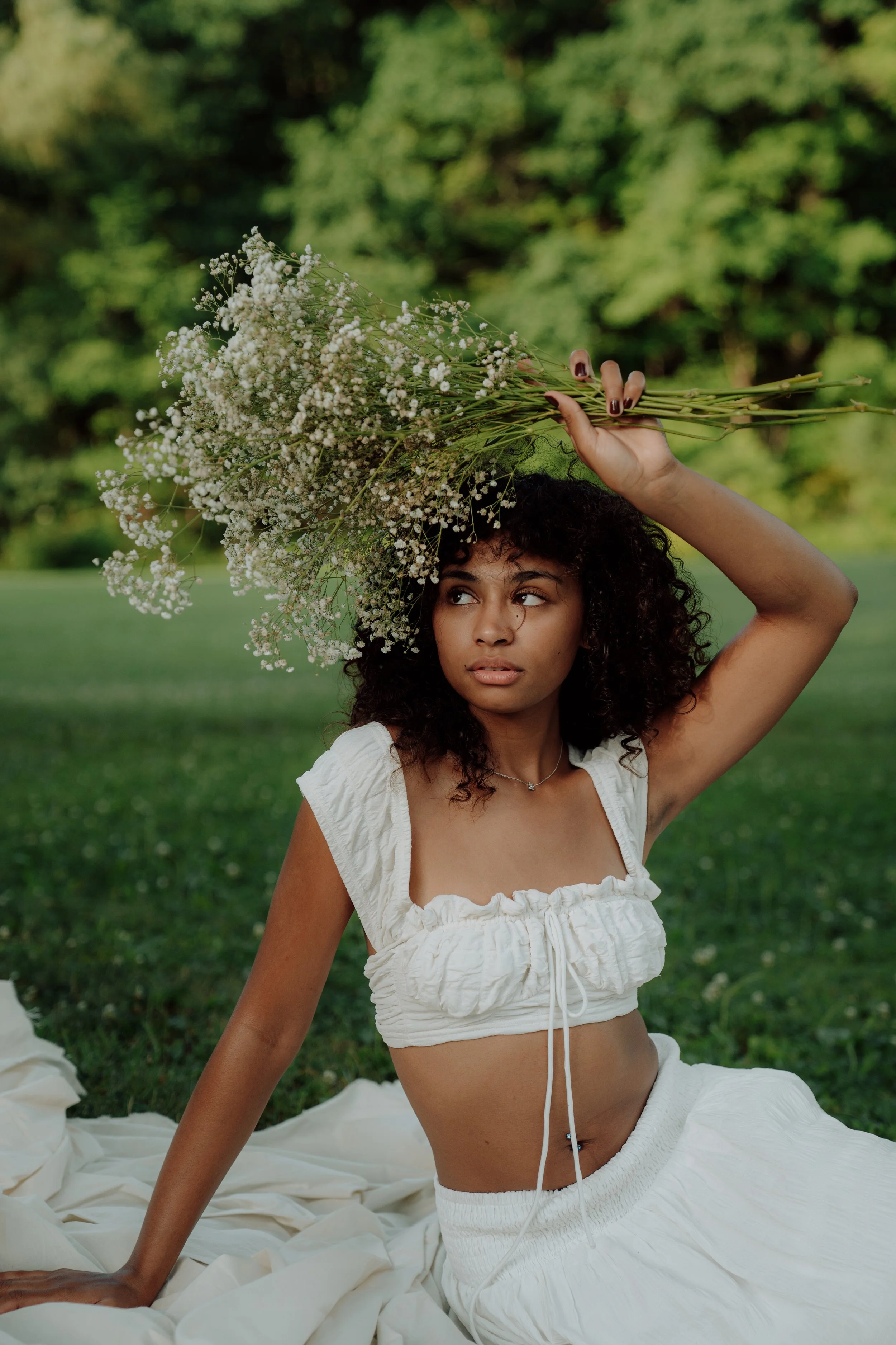 Young woman with curly hair holding a bouquet of white flowers outdoors.