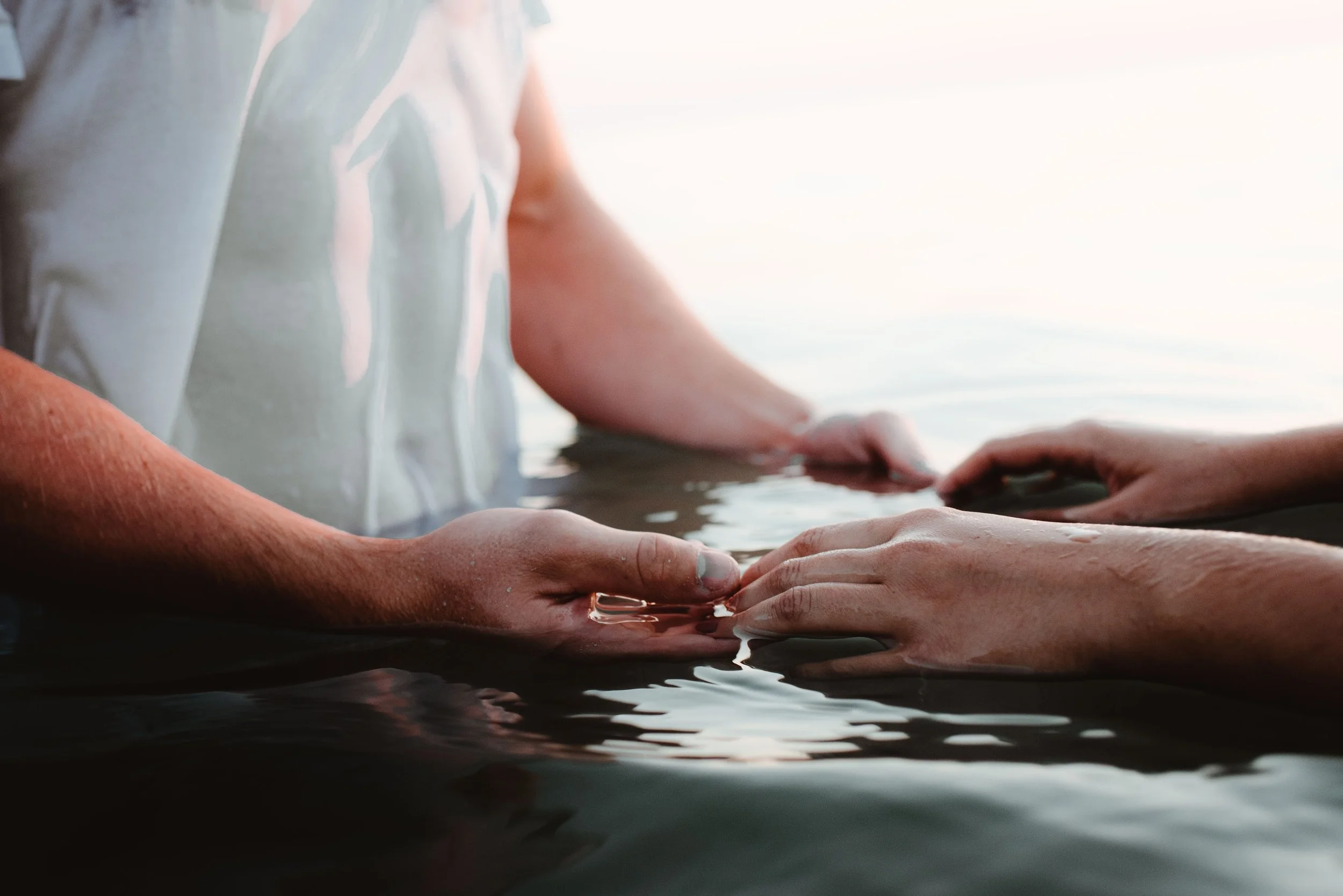 Person gently holding hands in water during sunset or sunrise.