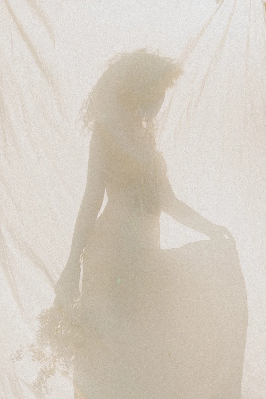 Silhouette of a woman sitting on a rock with her knees bent, against a bright background with light streaks.