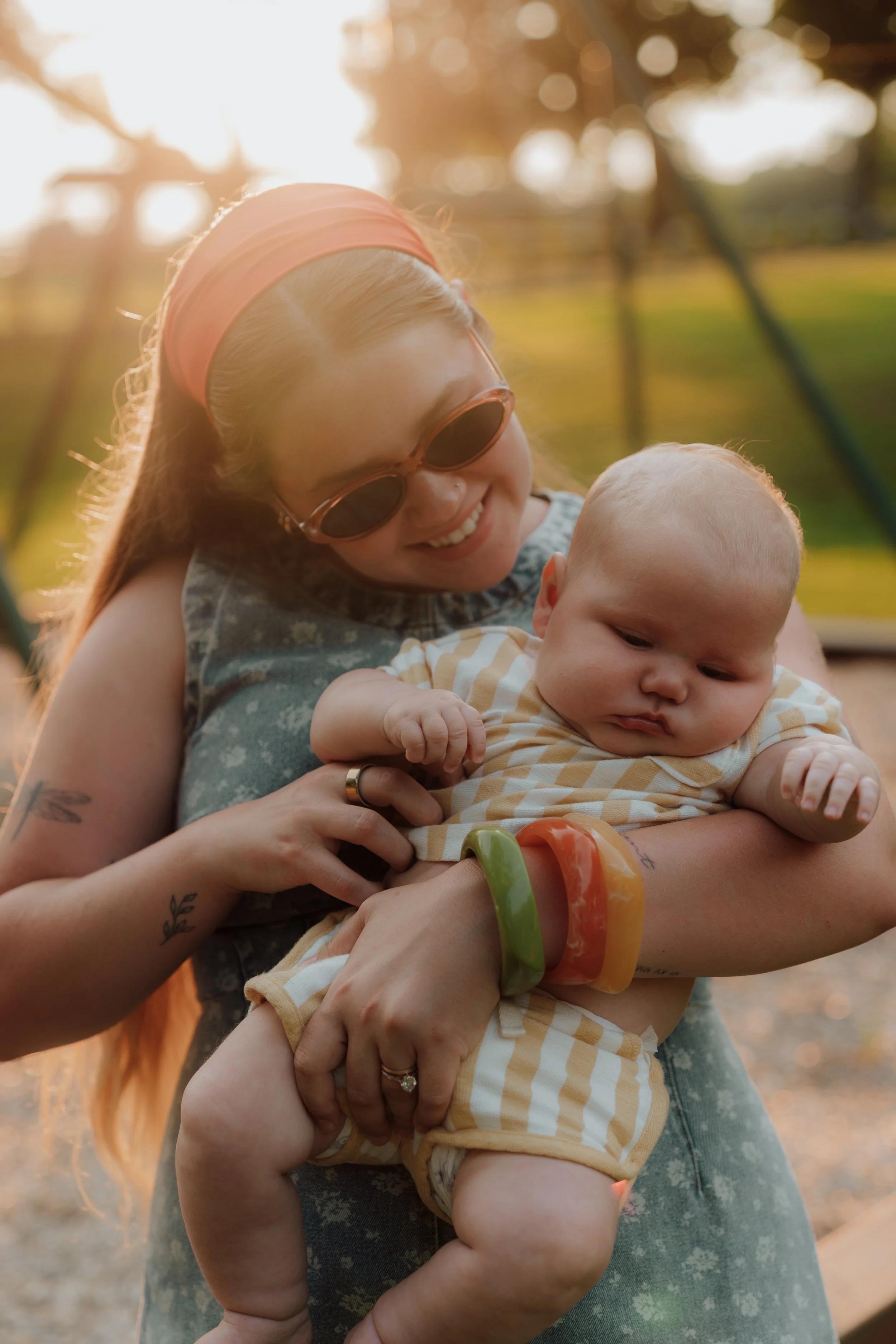 A woman smiling while holding a baby outdoors at sunset.