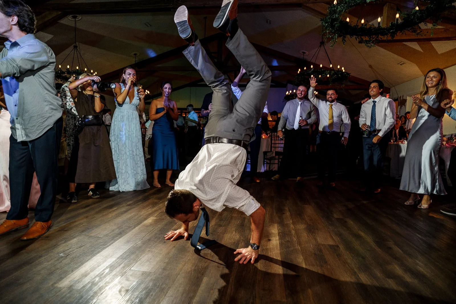 Man performing a handstand on the dance floor surrounded by guests at a celebration party.