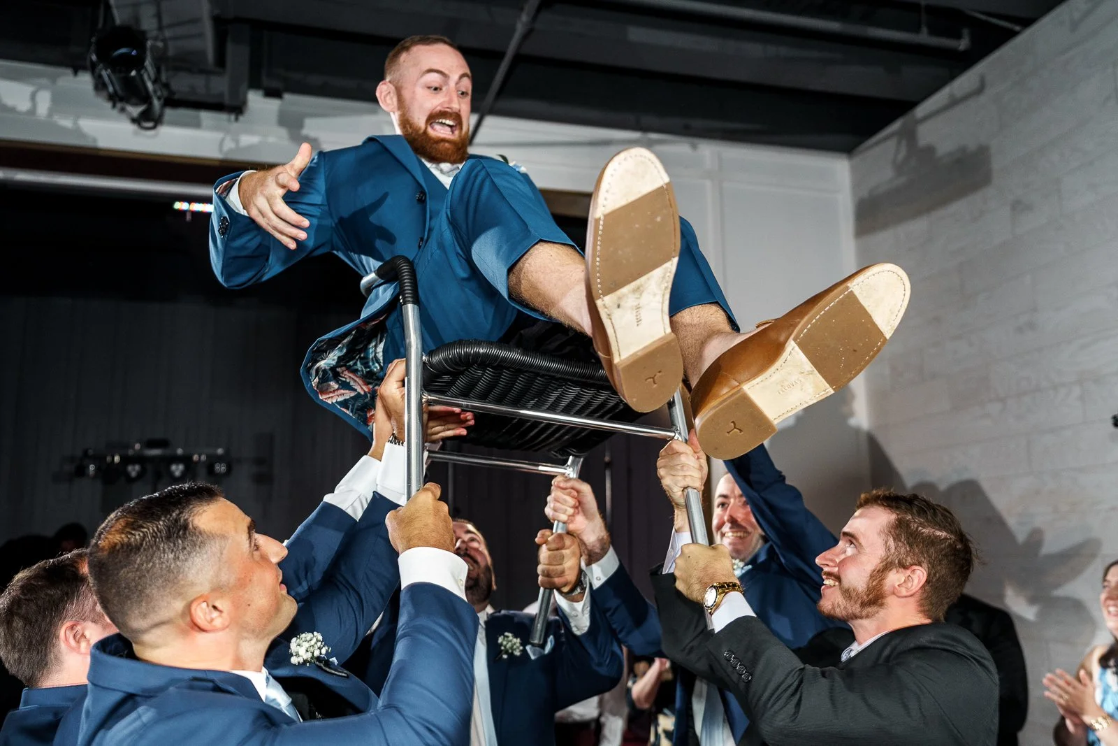 Groom being lifted on chair by friends at wedding celebration