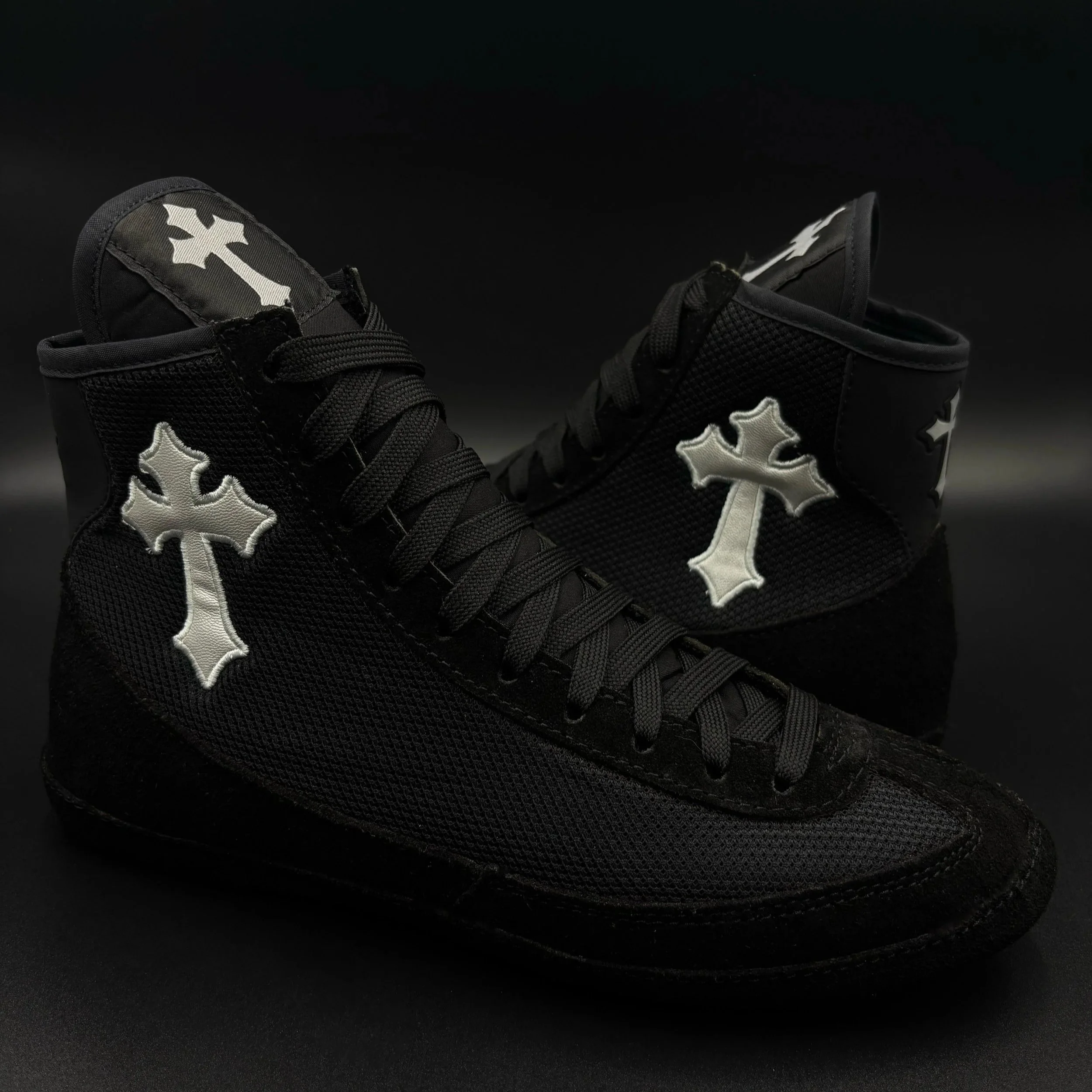 A pair of black sneakers with white star patterns and black laces on a dark surface.