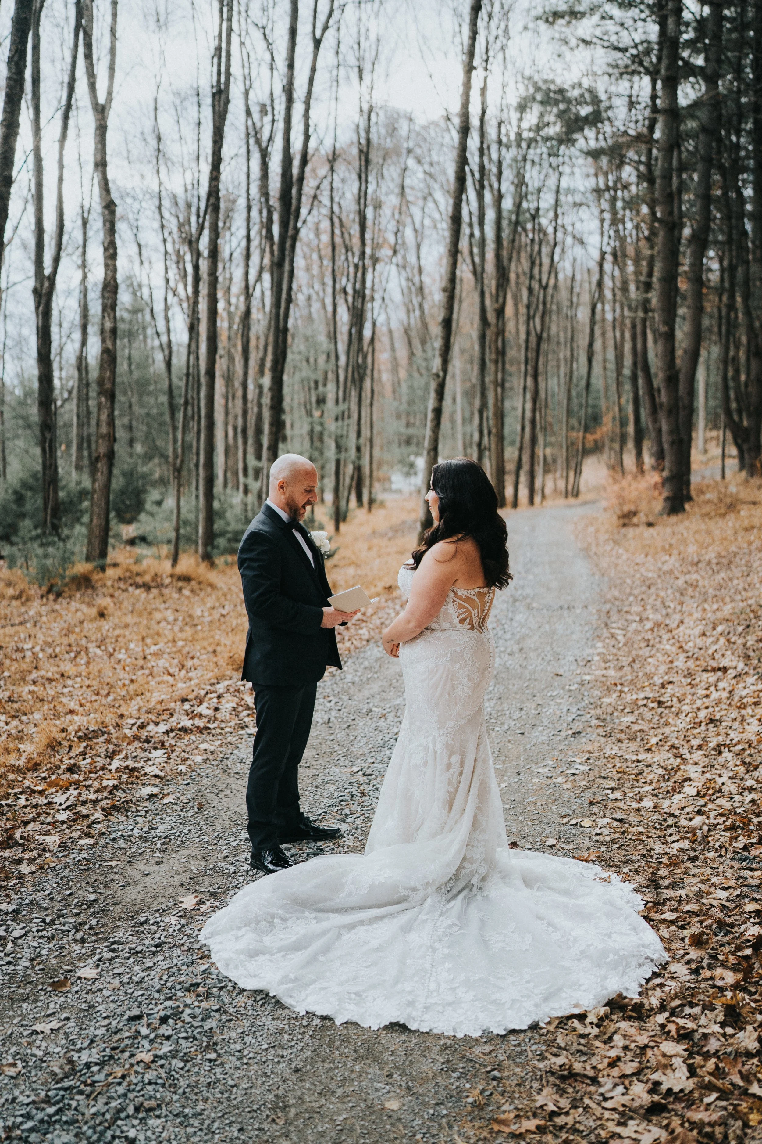 A bride and groom exchanging vows on a wooded forest path surrounded by fallen autumn leaves.