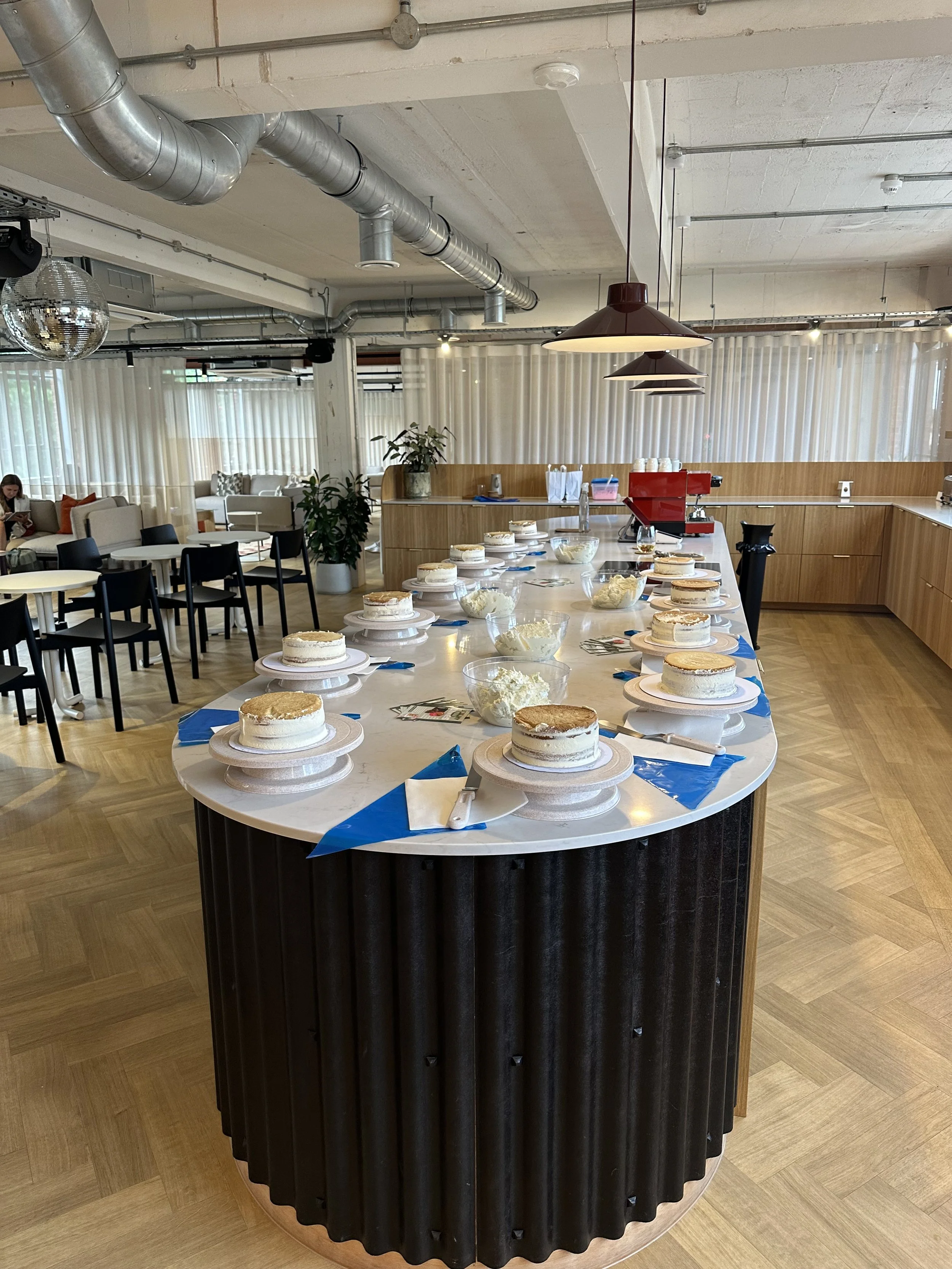 A restaurant or cafe with a curved island counter set up with multiple small cakes and utensils, ready for a cake tasting or celebration.
