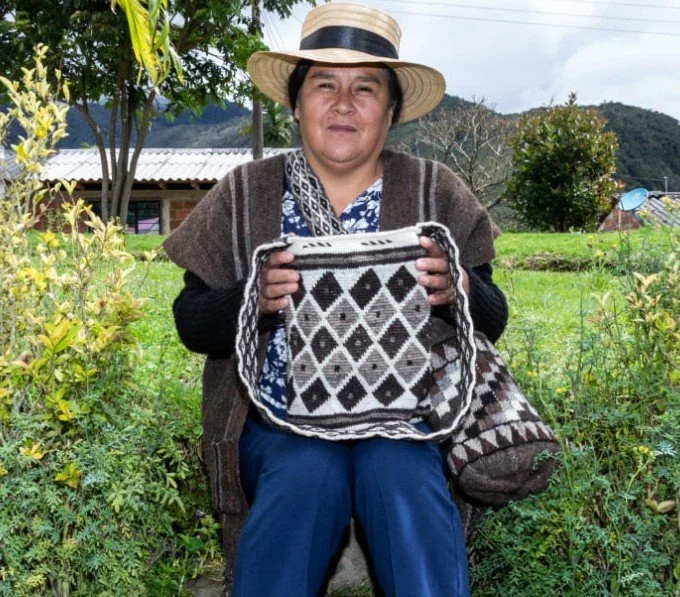 Colombia. Cauca region, Paez. Diva Eufemia is a weaver on the Cauca route. She is holding one of her creations: a bag (mochilla) in wool with tesselatng diamon motifs in white, grey, and black wool. Foto by Colombia Artesanal. Accessed via https://co