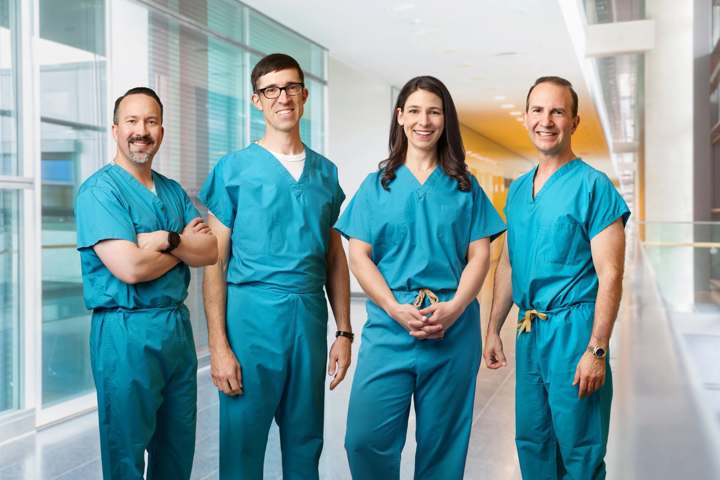Four medical professionals in blue scrubs standing in a hospital hallway, smiling for a photo.