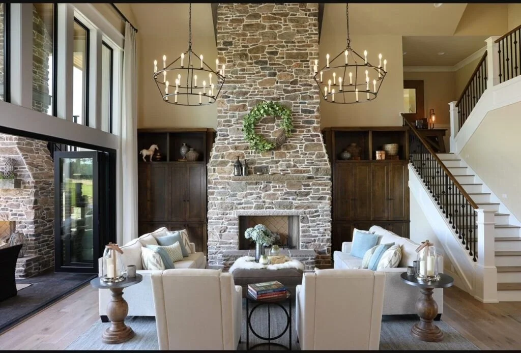 Living room with large stone fireplace, two chandeliers, and white sofas arranged around a coffee table.