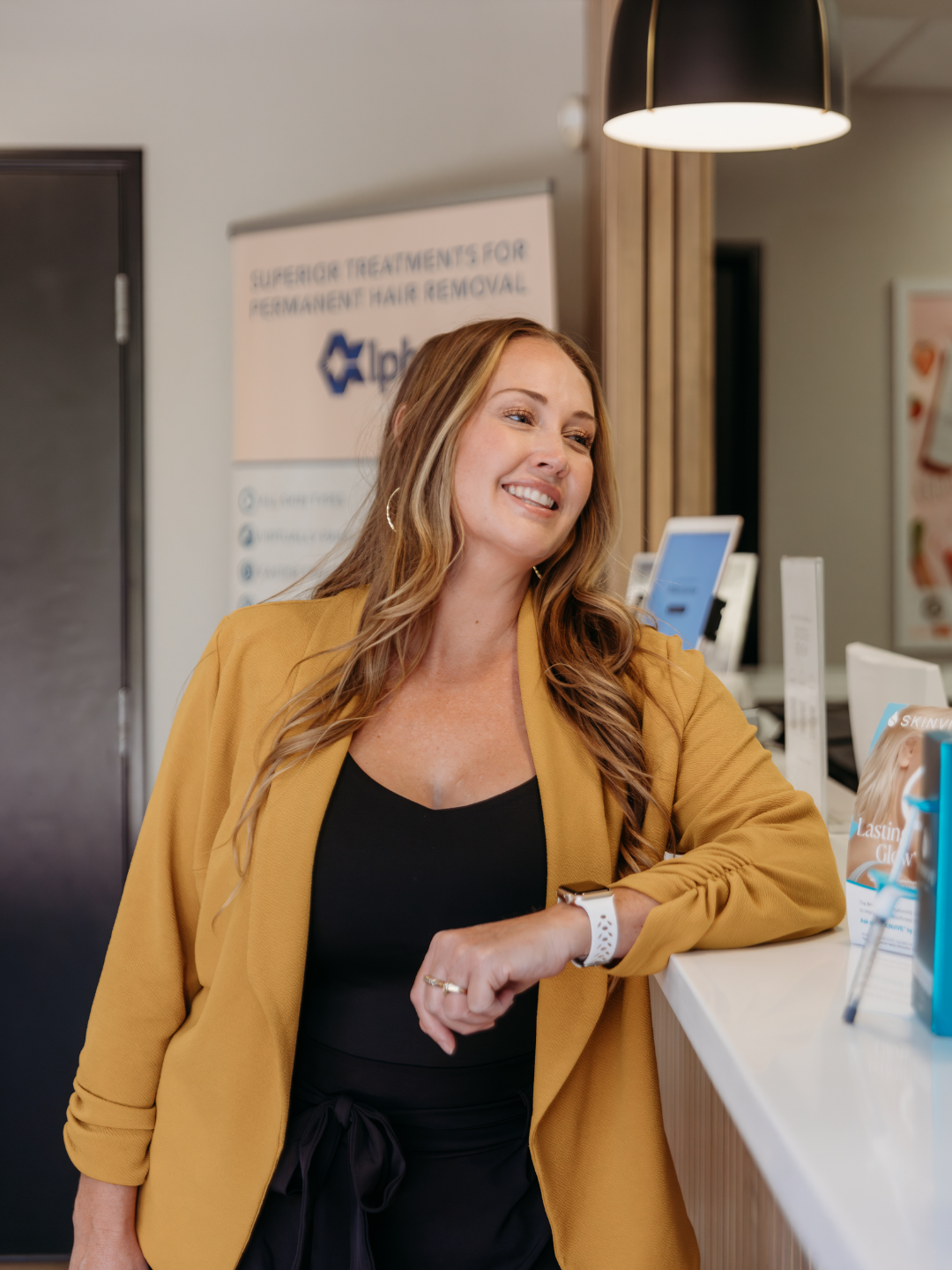 Katelyn, RN wearing a professional outfit leaning against the front desk in the lobby