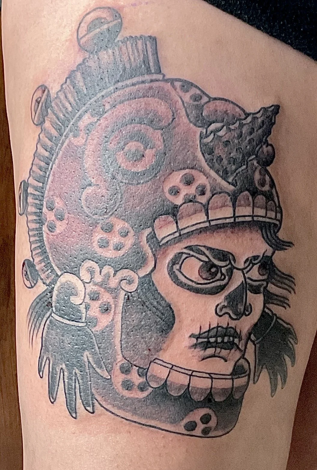Tattoo of a stylized skull with a mohawk, angry eyebrows, sunglasses, a mustache, and various decorative patterns.