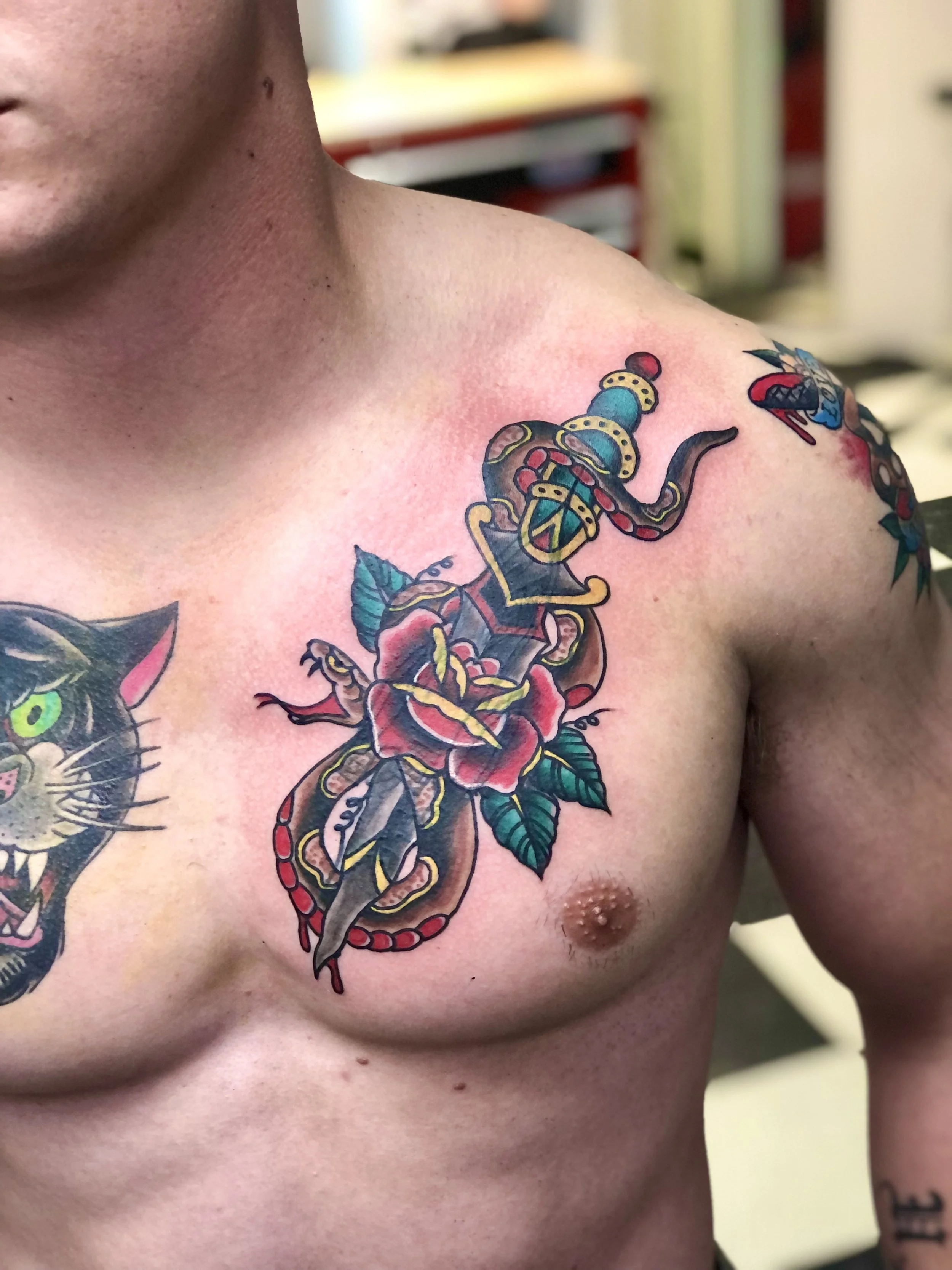 Tattoo of a snake intertwined with a red rose and green leaves on a man's chest.