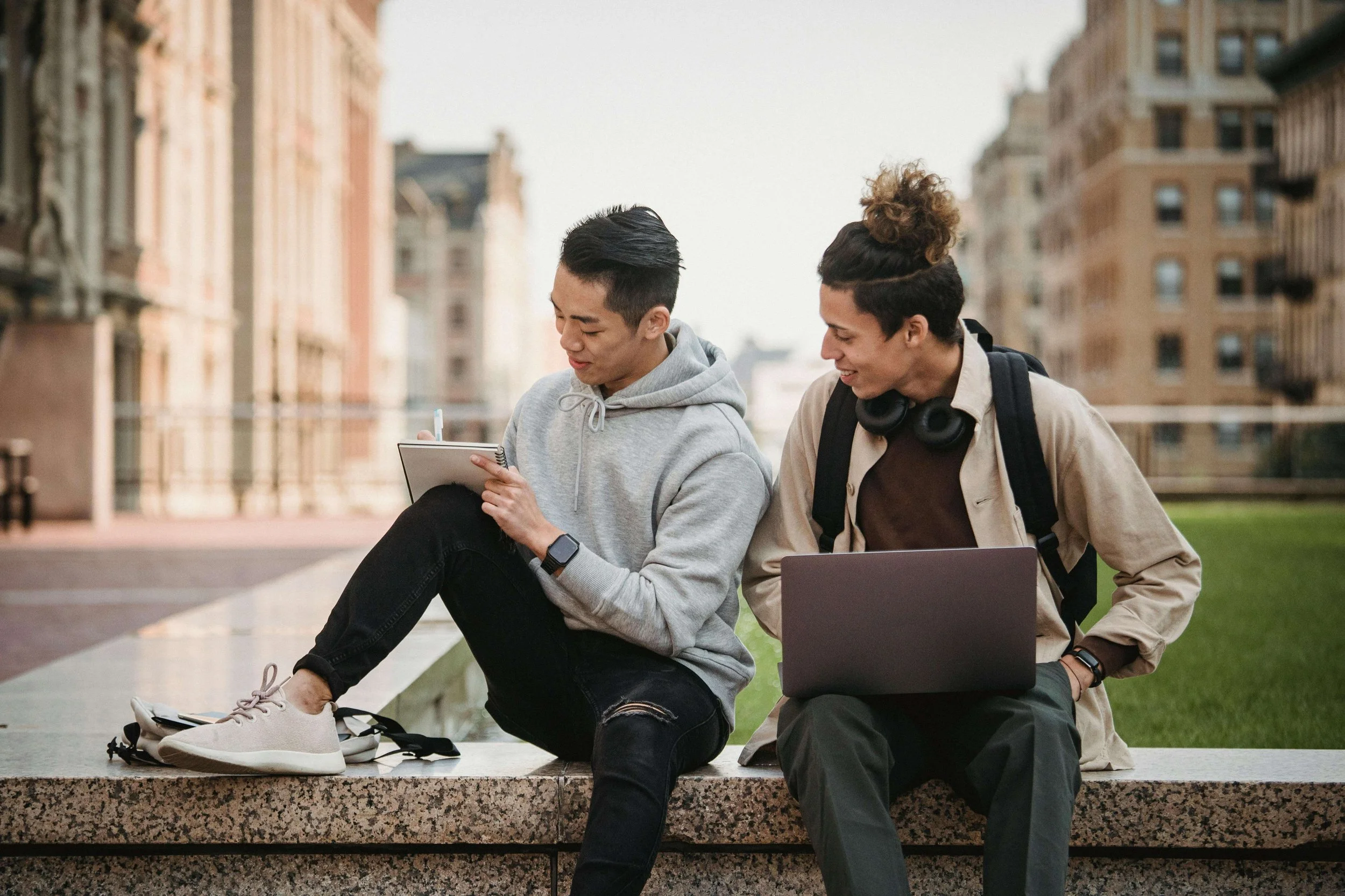Two young adults sitting together outdoors with notebooks and a laptop, showing connection that can still feel lonely without support like depression therapy for young adults in West Babylon, NY.