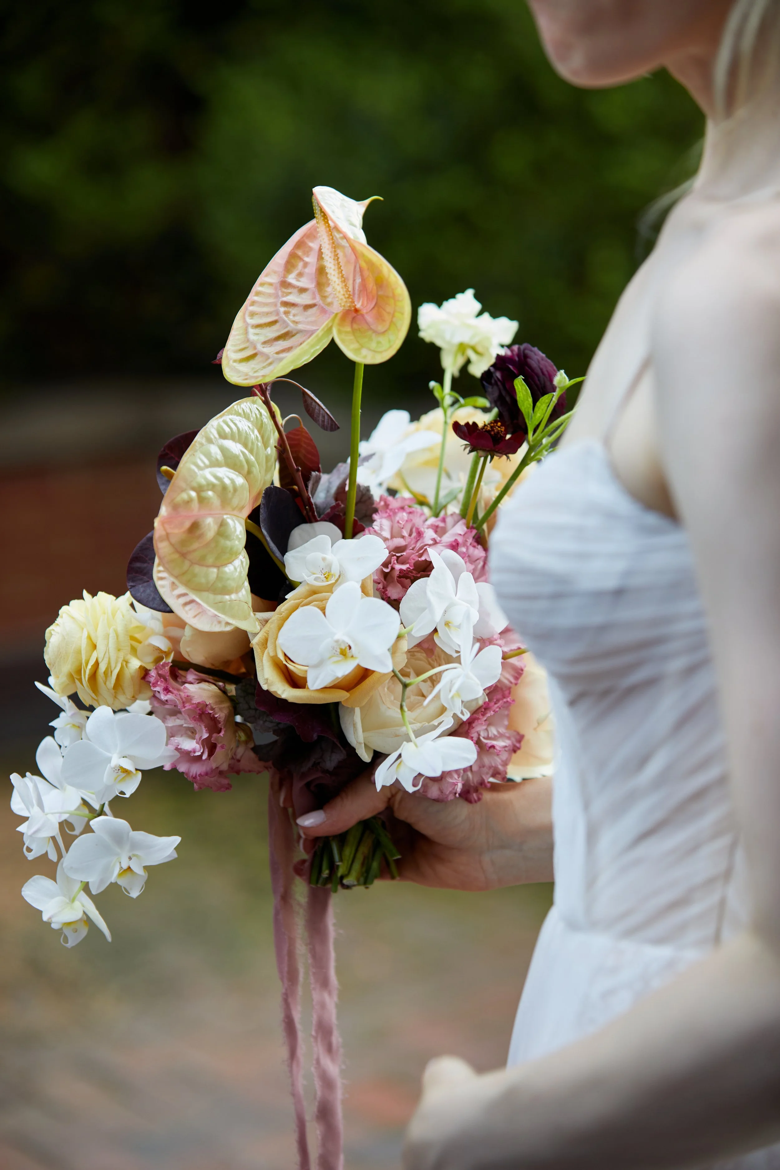 Bride holding a colorful bouquet featuring white, pink, and yellow flowers with green foliage.