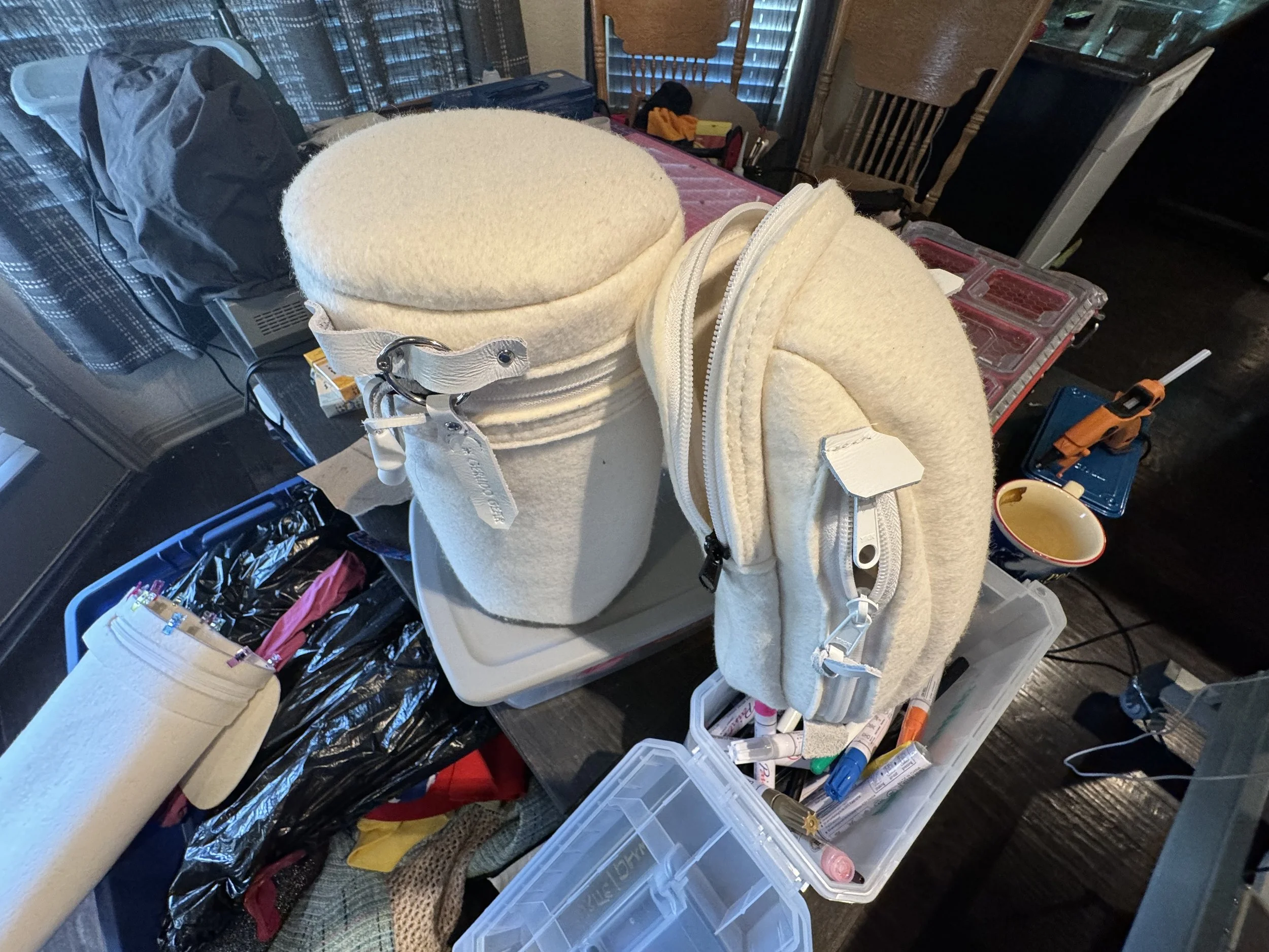 Various felt and fabric rolls, makeup brushes, and tools on a cluttered table, with bags and other storage containers in the background.