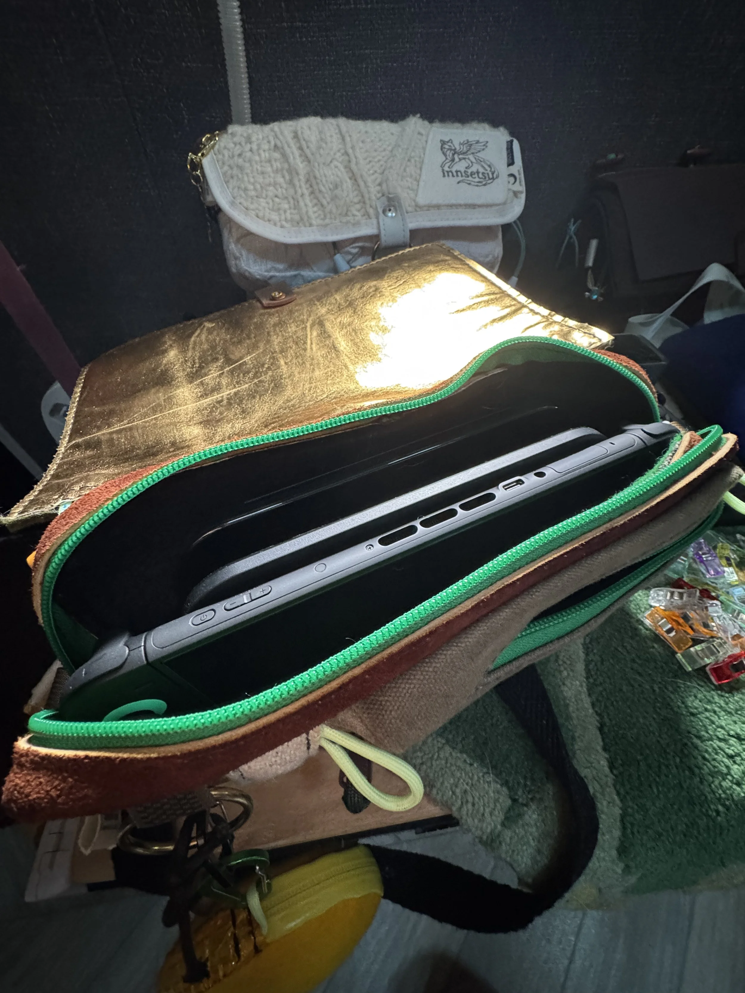 Open bag with a laptop inside, resting on a surface near a green bag with keychains, a white knitted pouch, and some small items.