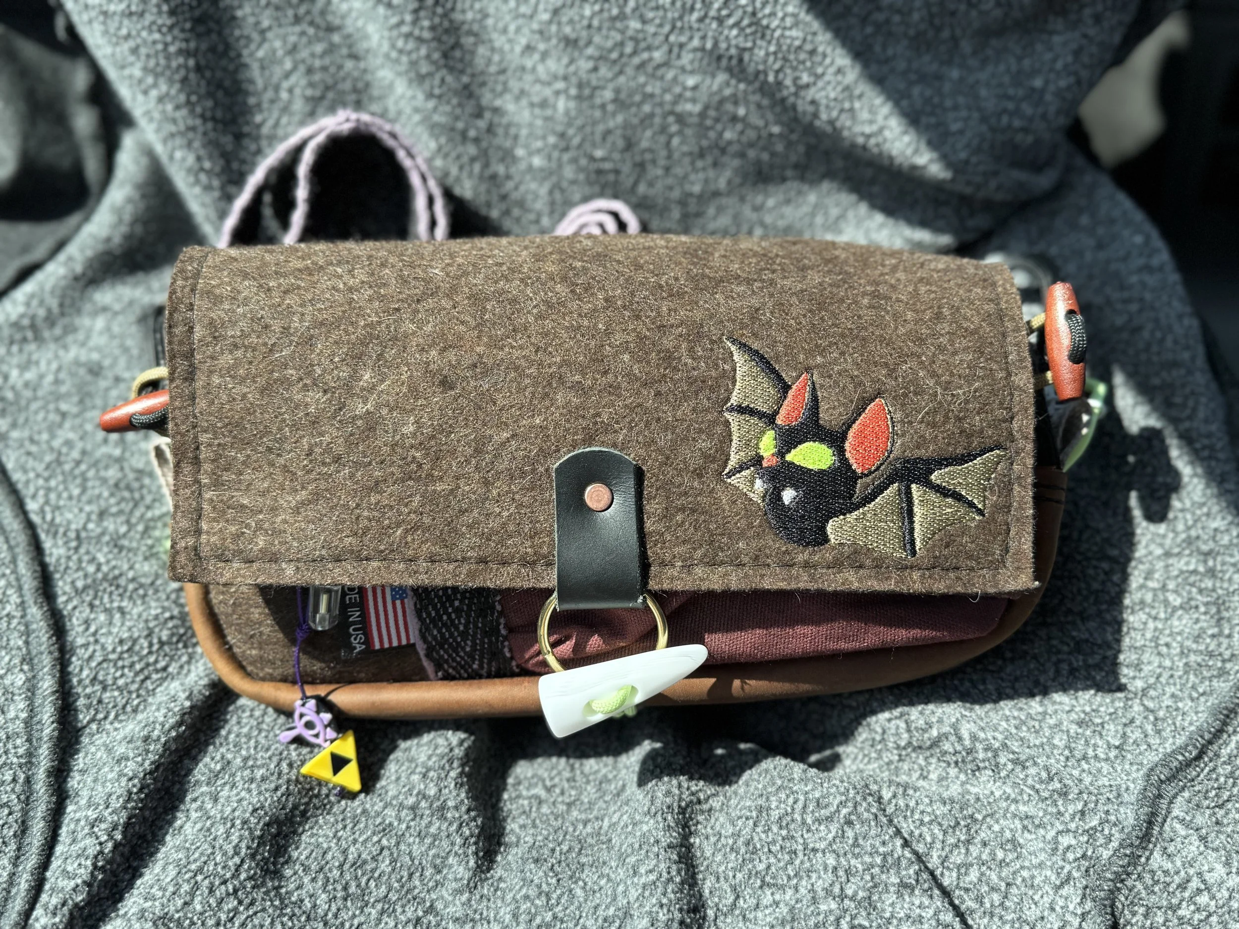 A brown fabric bag with an embroidered bat design, resting on a gray textured surface.