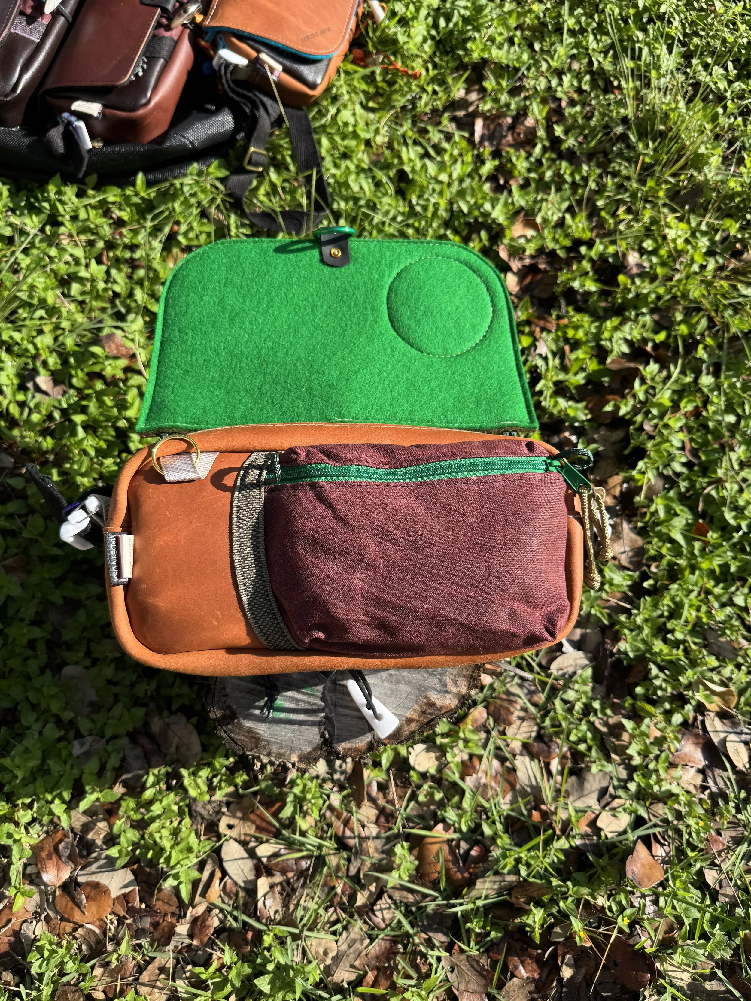 Open backpack with a brown and green design, placed on a tree stump outdoors, surrounded by green plants and fallen leaves.