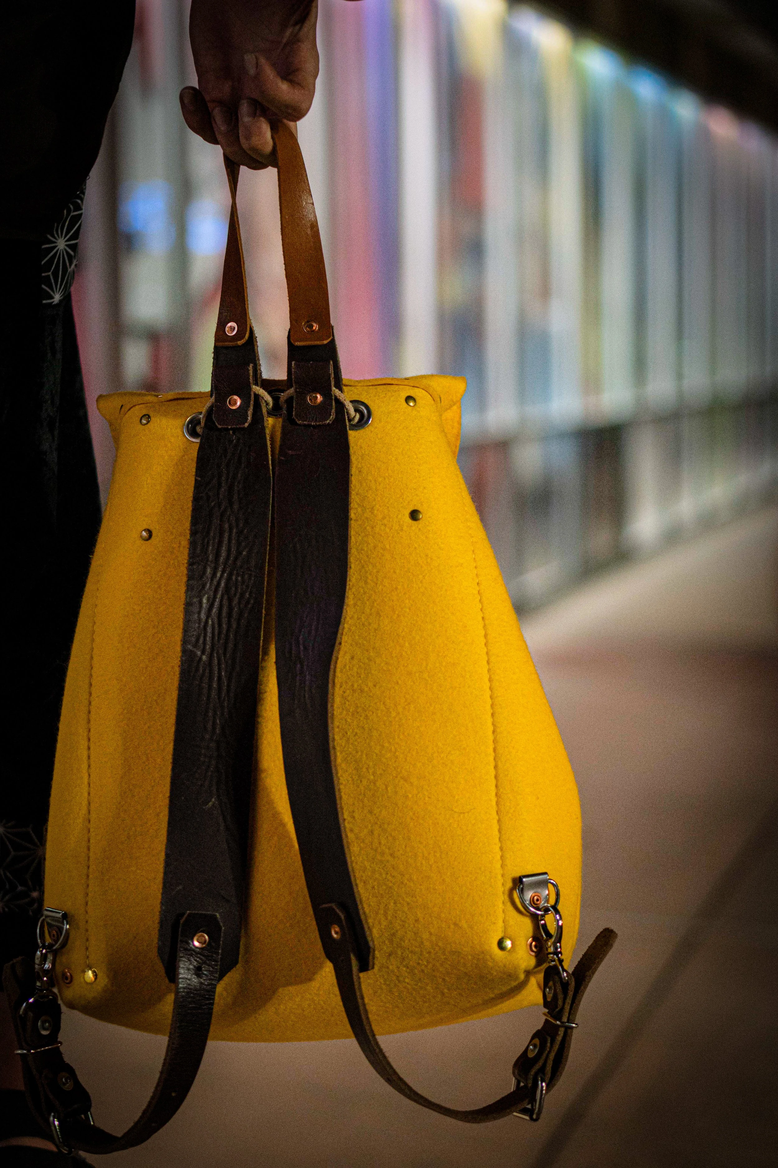 Person holding a yellow handbag with brown straps in a library or bookstore aisle.