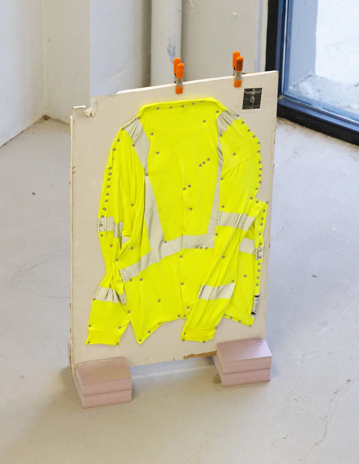 Mr. Universe (2025) (view 2) drywall, ink, found images, inkjet prints, gaffers tape, painters tape, cellophane tape, caution tape,  thumb tacks, Carhartt Hi-Vis long-sleeved shirt, polystyrene insulation foam, and clamps