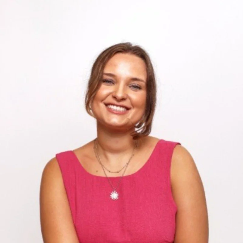 Gabi, Rachel's client has short brown hair, smiling, wearing a pink sleeveless top and two necklaces, standing against a white background.