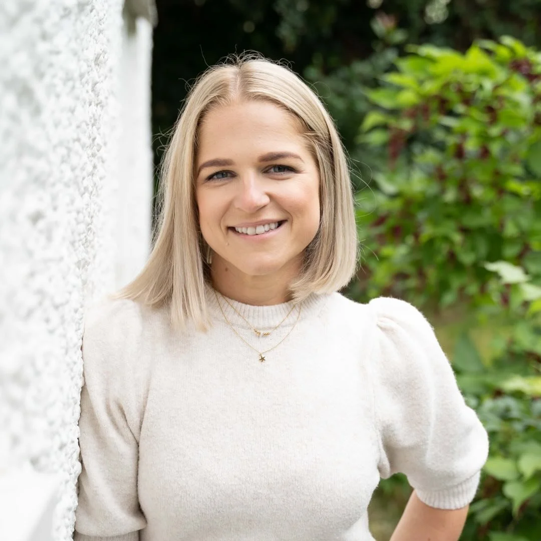 Emily, Rachel's client, has blonde hair smiling outdoors, wearing a white sweater and layered necklaces.