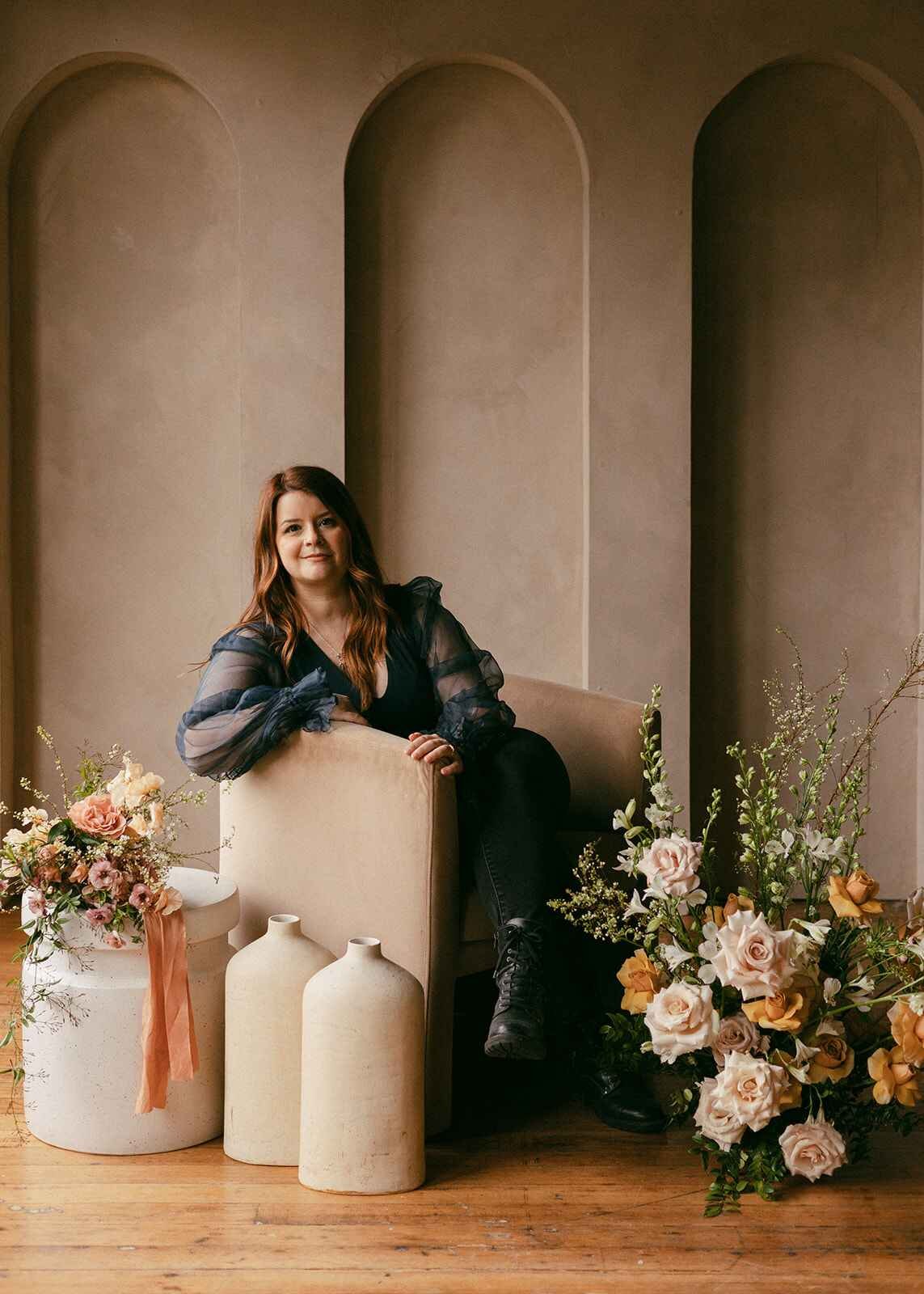 Founder of Moonflower Design Co sitting in chair and looking at camera with flowers next to her.
