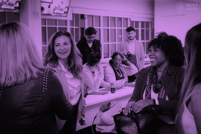 Group of diverse women and men engaged in conversation at an indoor social gathering, with smiling faces.