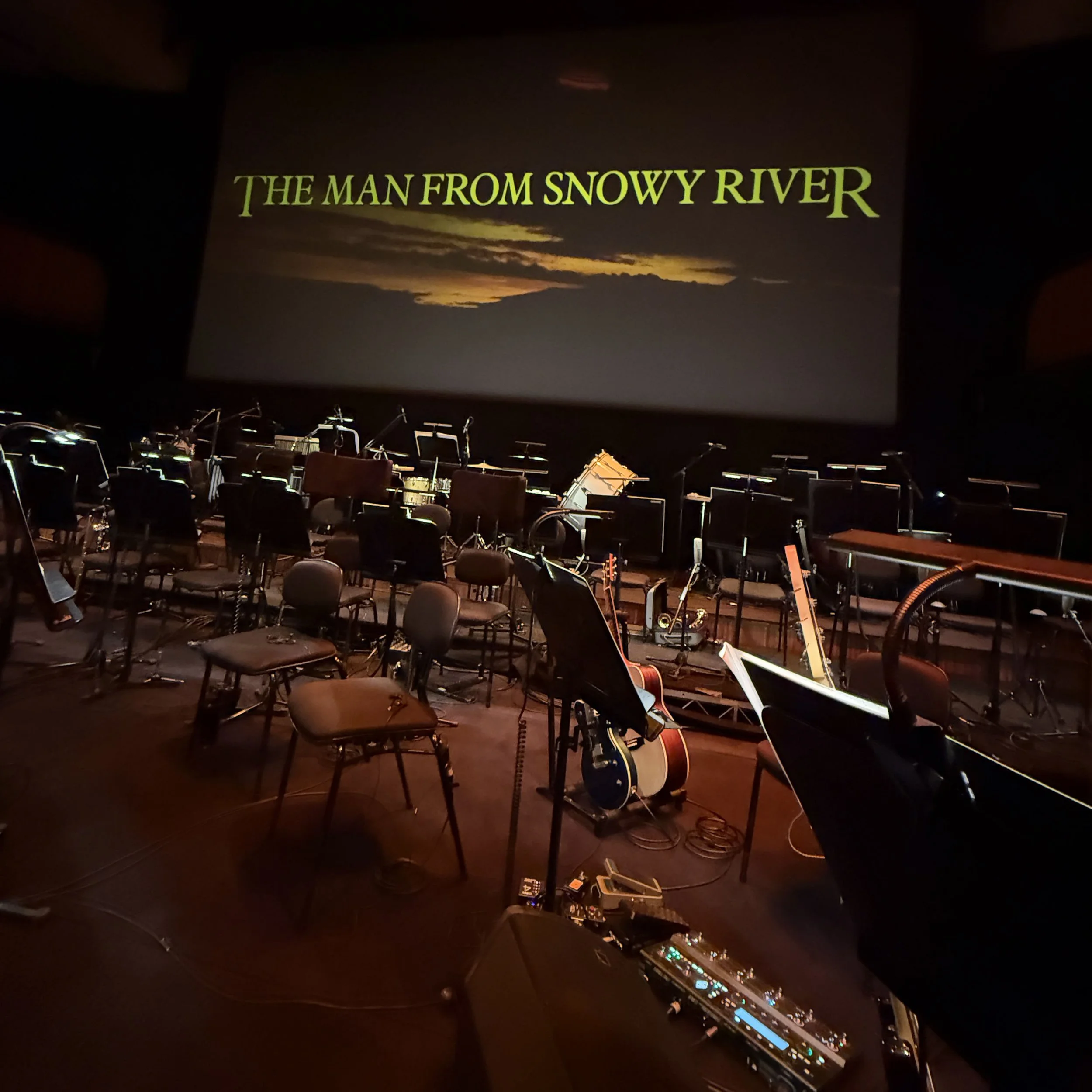 Stage shot at the Sydney Opera House from  'The Man From Snowy River'. The theater seats and musical instruments like guitars and music stands are visible in the dimly lit room.
