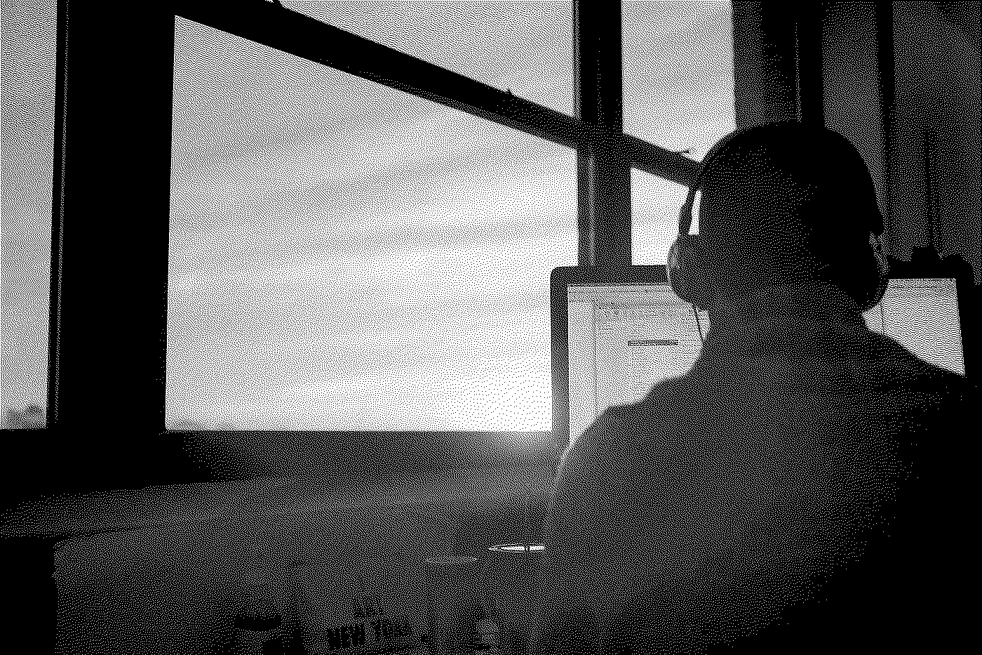 Silhouette of a person wearing headphones working on a computer at a desk, with sunlight coming through a window.