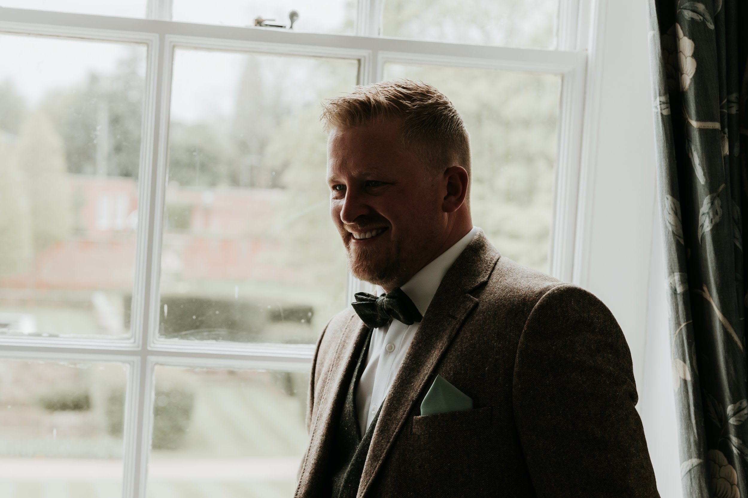 Smiling man in a suit with bow tie standing by a window.