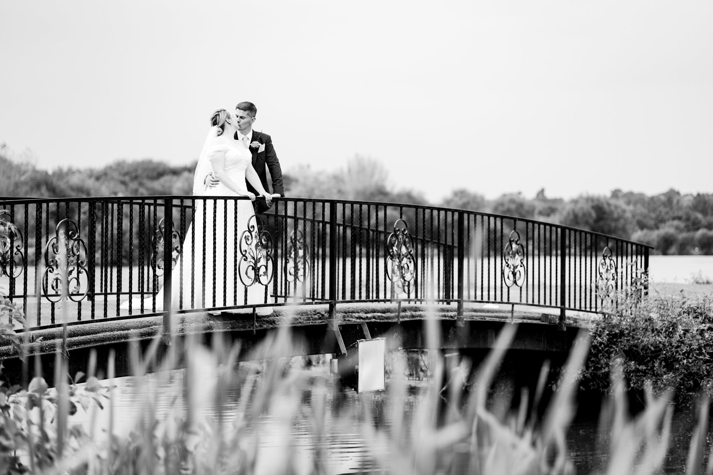 Bride and groom on a decorative metal bridge over water, black and white photo.