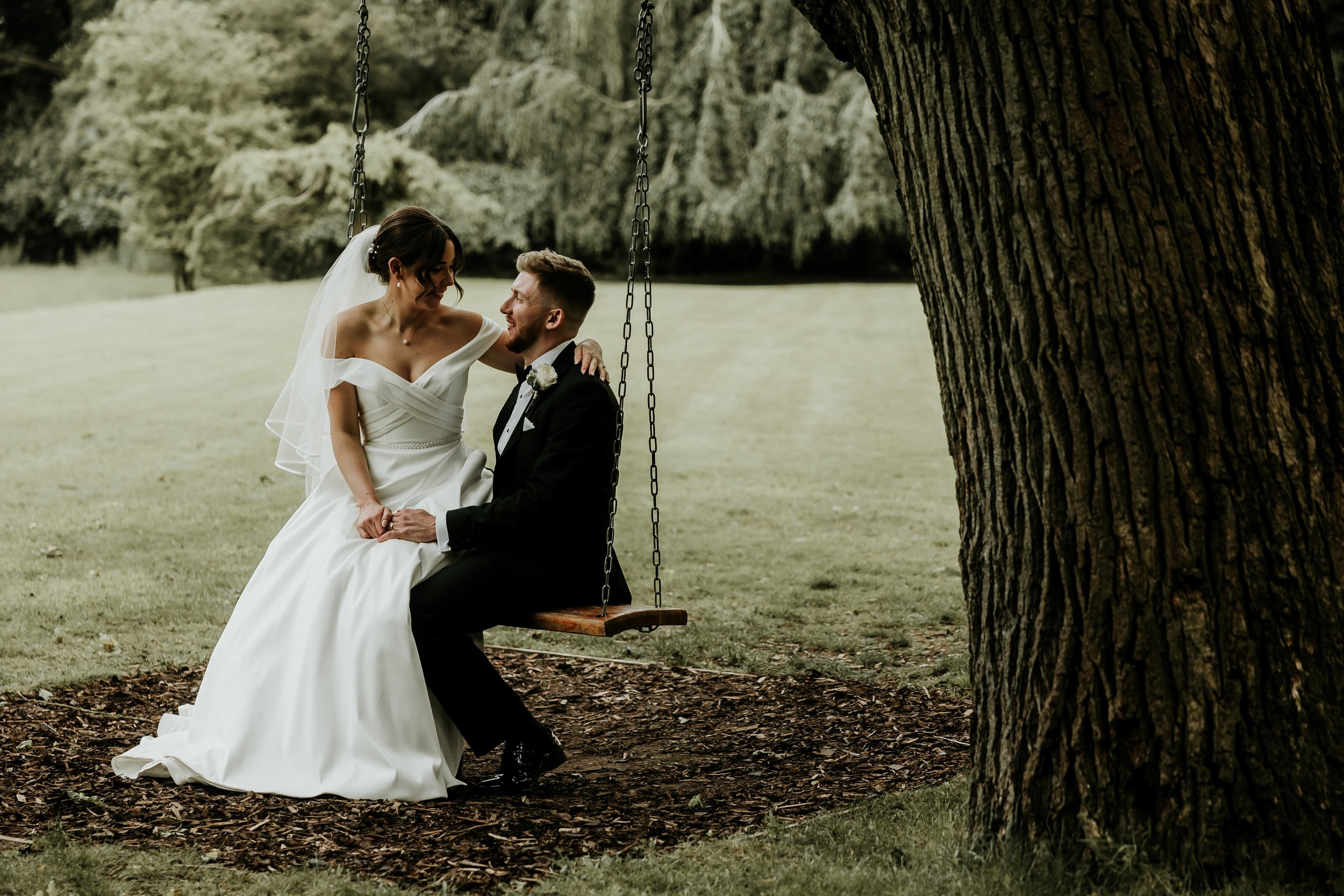 Bride and groom on a swing under a tree.