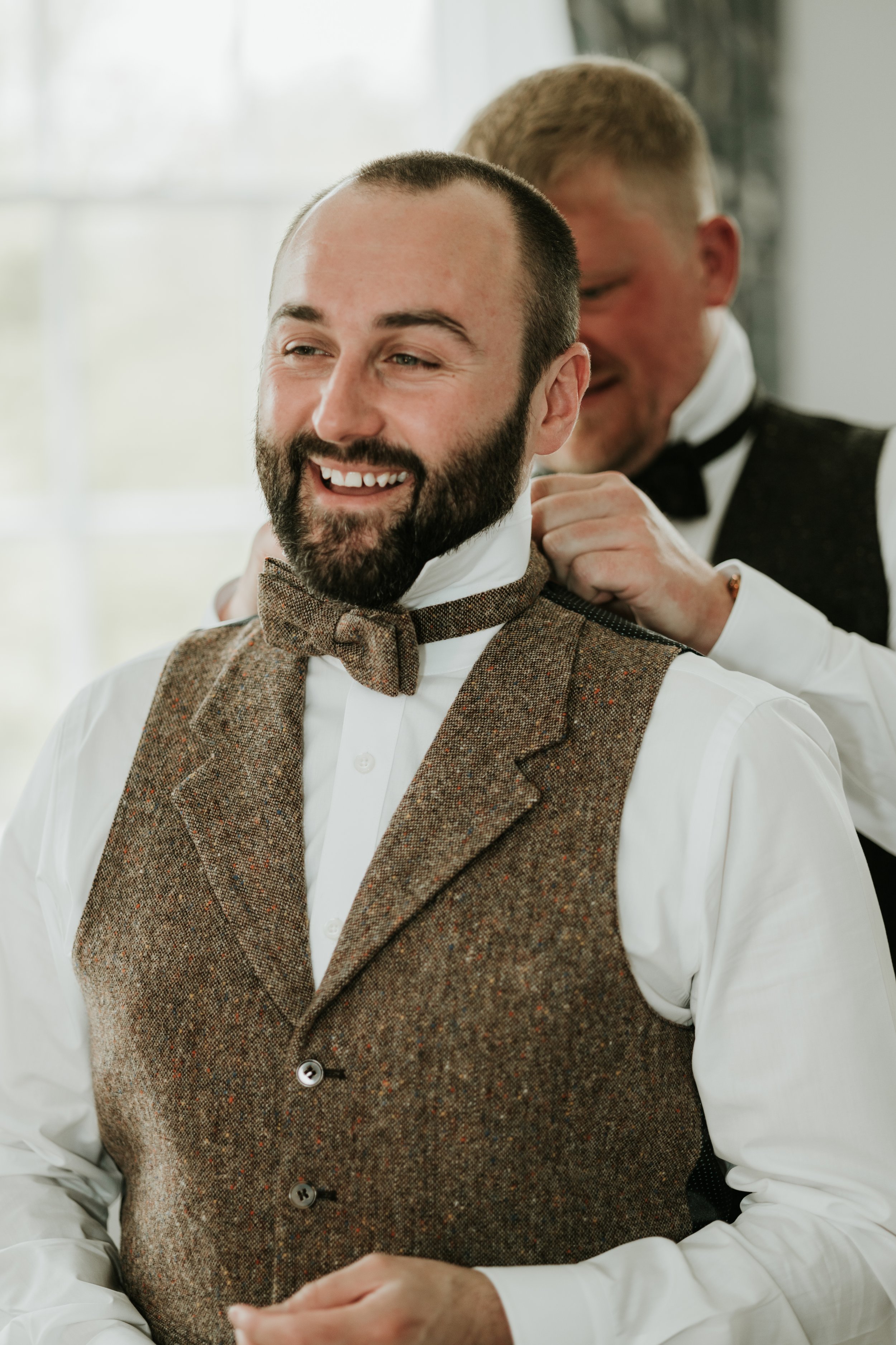 Man adjusting another man's bow tie in formal attire.