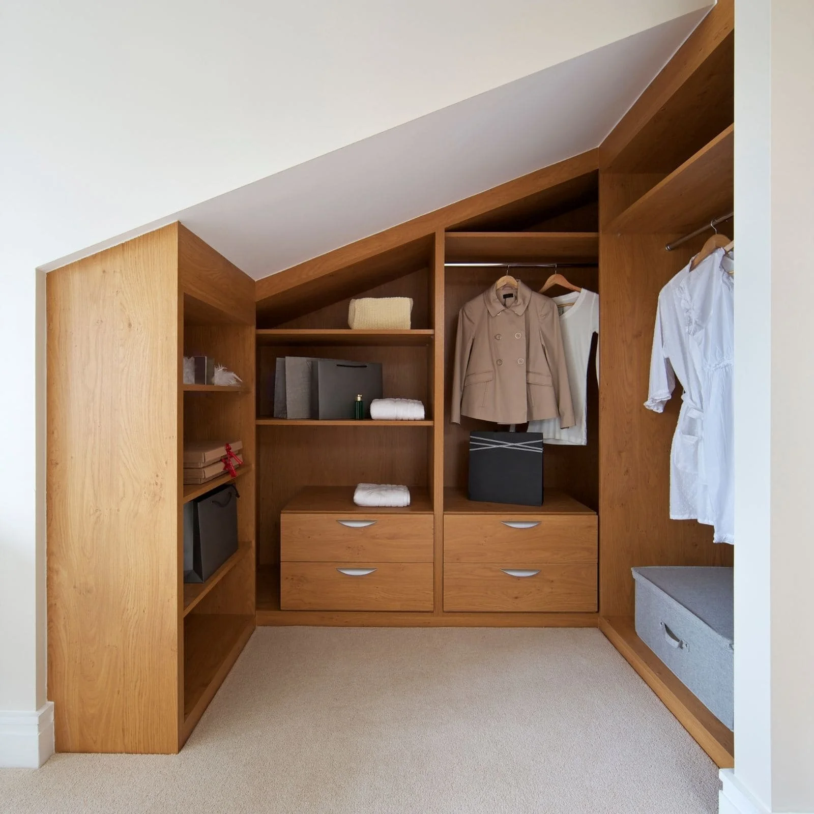 Dressing sur mesure en bois conçu sous une pente de toit avec penderies, étagères et tiroirs afin d'optimiser l'espace dans des combles.