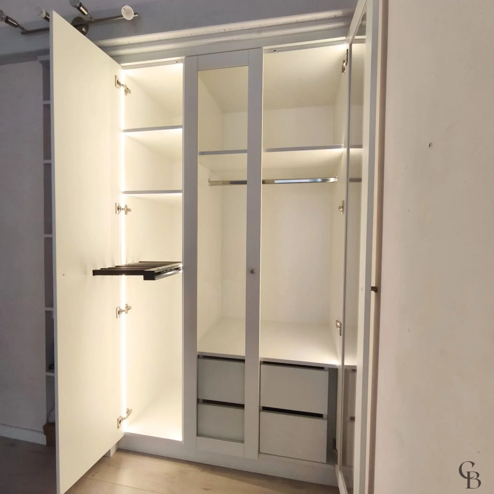Dressing sur mesure avec portes ouvertes, éclairage LED intégré, miroir central, tiroirs et penderies réalisé par Concept & Bois à Genève.