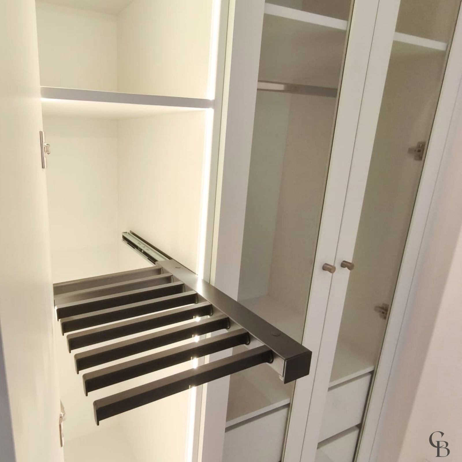 Détail d'un dressing sur mesure avec porte-pantalons coulissant, éclairage LED intégré et rangements haut de gamme réalisé par Concept & Bois à Genève.