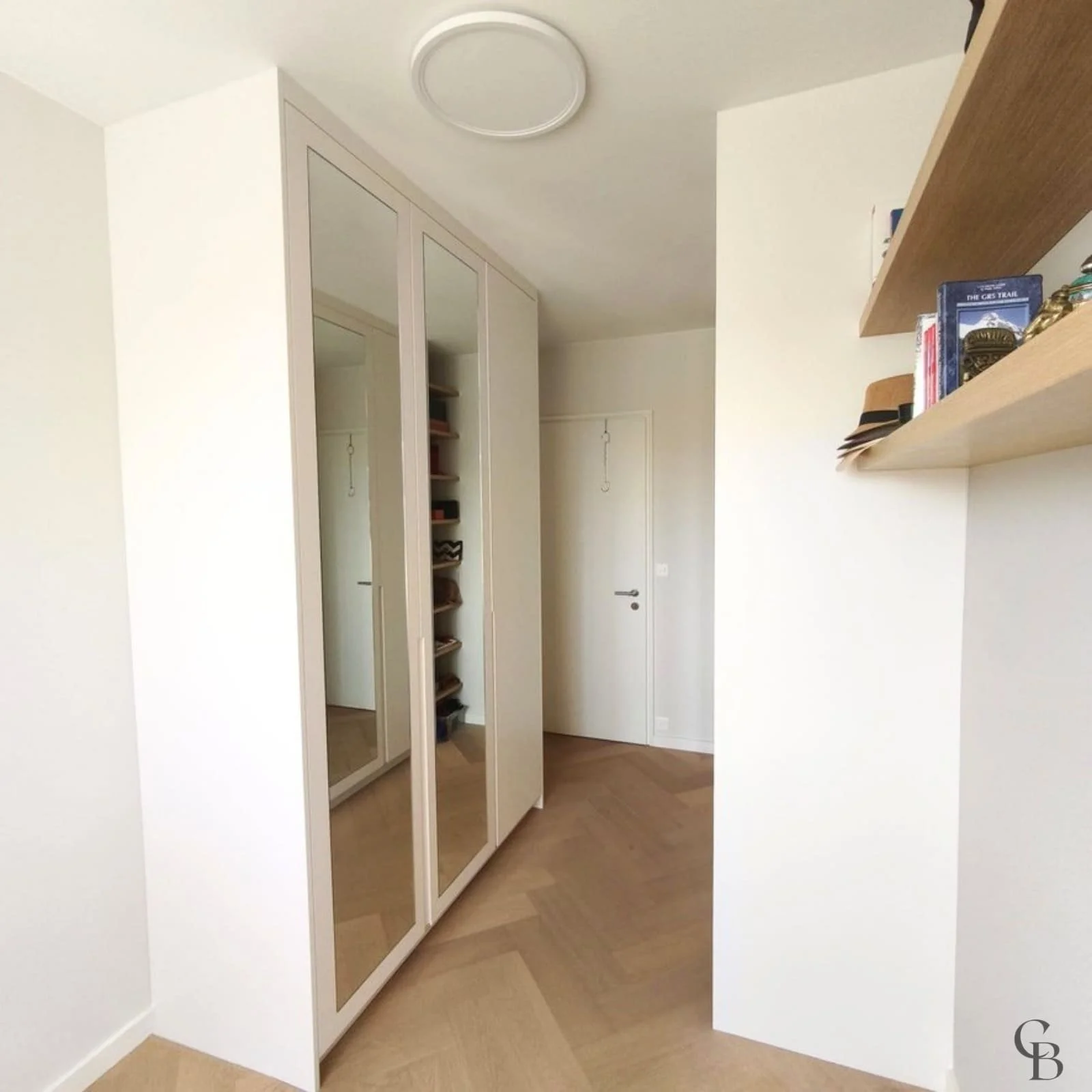 Cette vue d'ensemble met en valeur l'intégration parfaite de l'armoire sur mesure réalisée par Concept & Bois. Les portes miroir agrandissent visuellement la pièce tandis que les rangements intégrés offrent une organisation optimale et un design sobr
