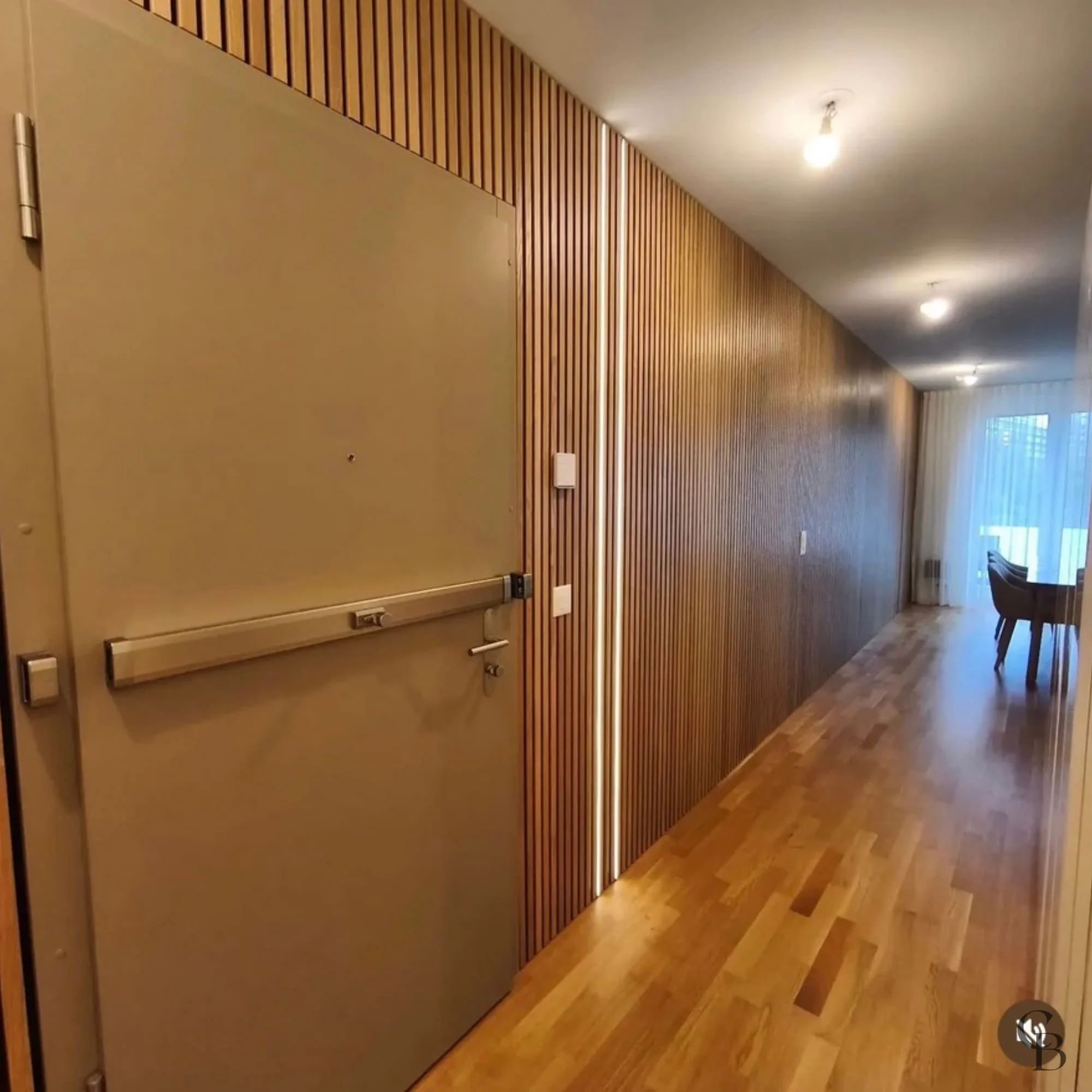 Habillage mural en tasseaux de bois avec porte invisible intégrée et éclairage LED, réalisé sur mesure pour créer une entrée élégante, chaleureuse et parfaitement intégrée à l'architecture intérieure.