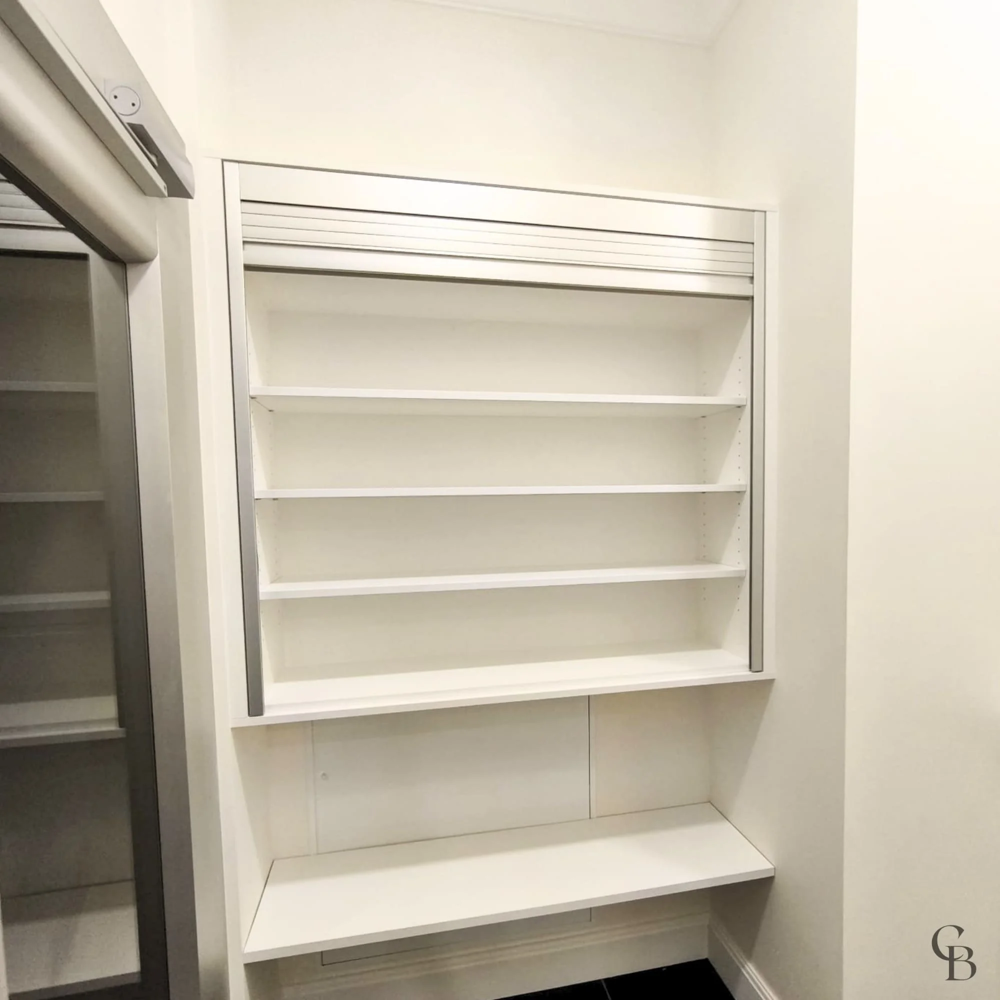 Espace de rangement sur mesure équipé d’un volet roulant et d’étagères personnalisées.