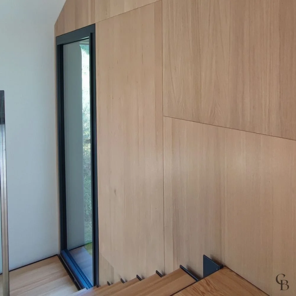 Habillage mural en bois réalisé sur mesure avec intégration discrète des portes et des rangements, offrant une continuité parfaite entre les différents espaces de la maison.