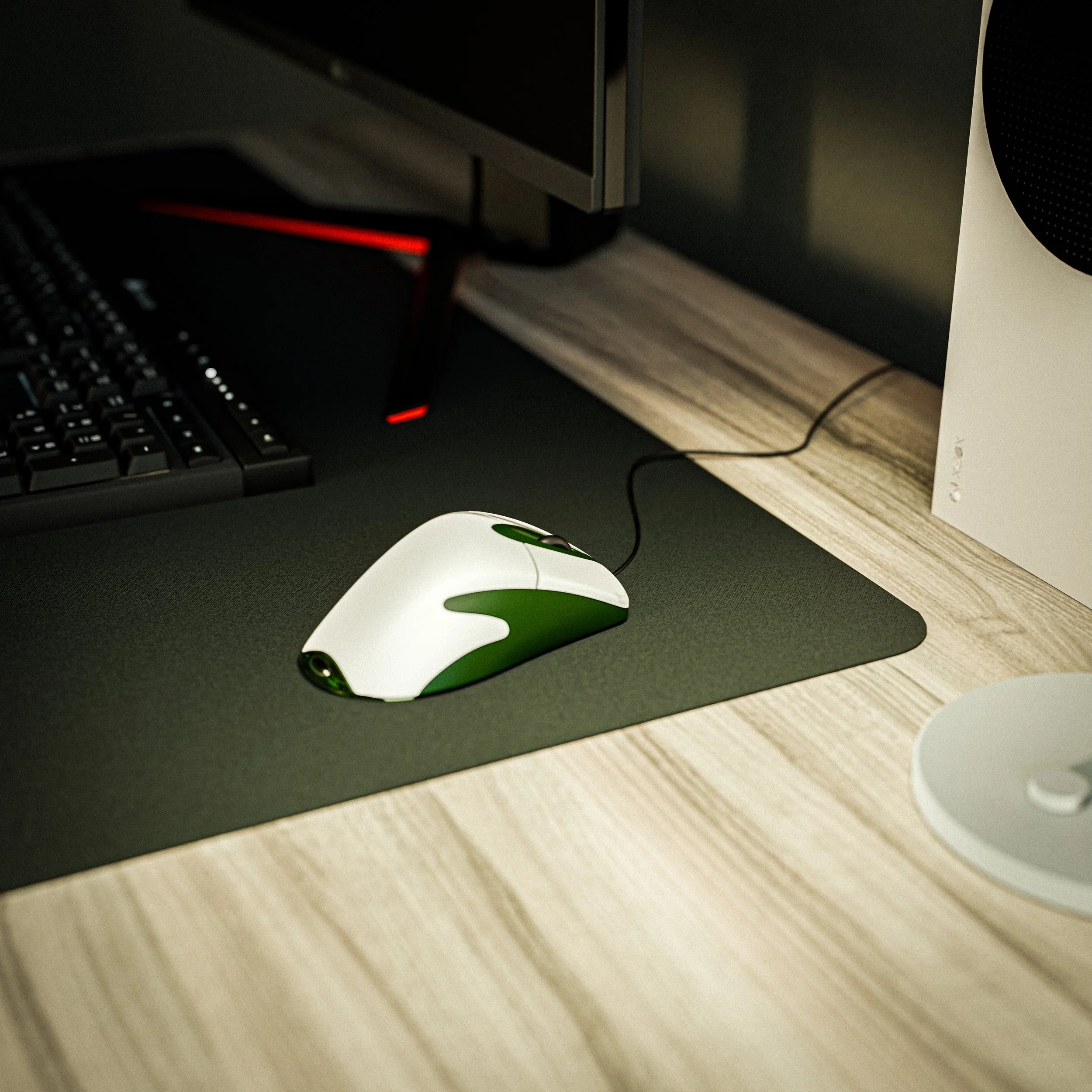 Souris d'ordinateur blanche et verte sur un tapis de souris noir, à côté d'un clavier noir, d'un écran et d'une enceinte blanche sur un bureau en bois.