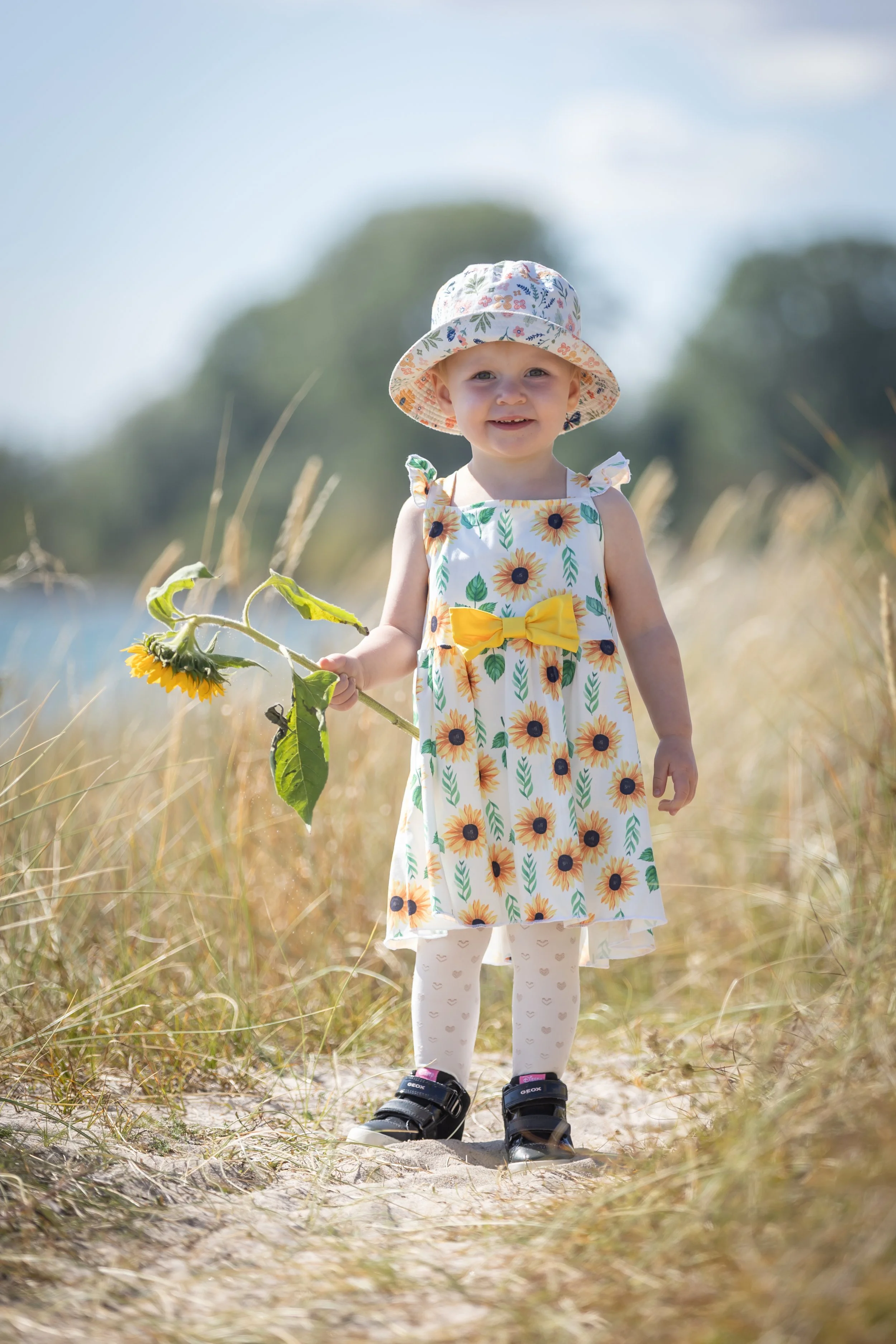 Barn- och familjefotografering i Skåne – leende barn i sommarklänning på strandäng i mjukt dagsljus