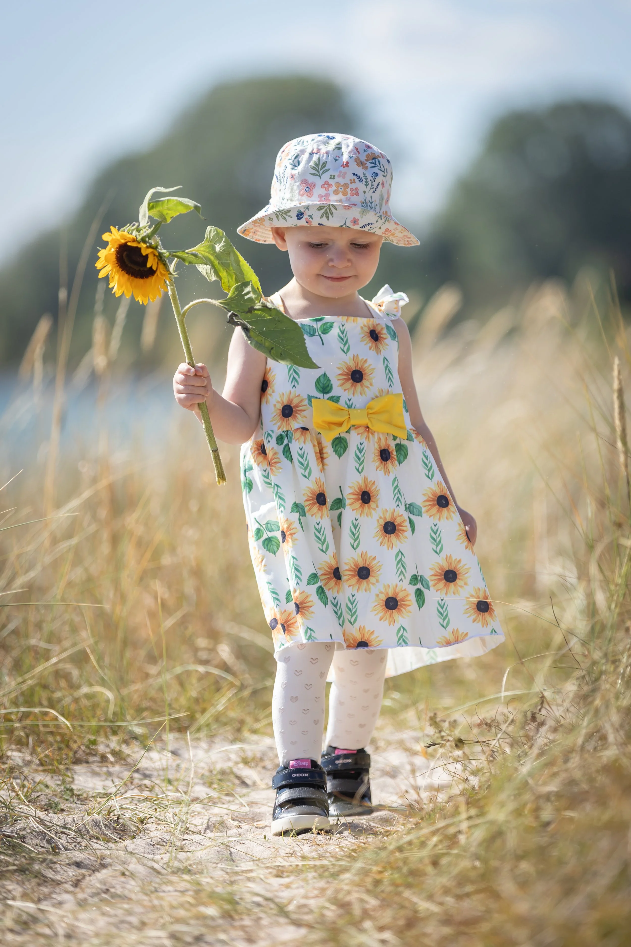 Barnfotografering i Ystad – litet barn i somrig klänning med solros, fotograferad utomhus i naturligt ljus