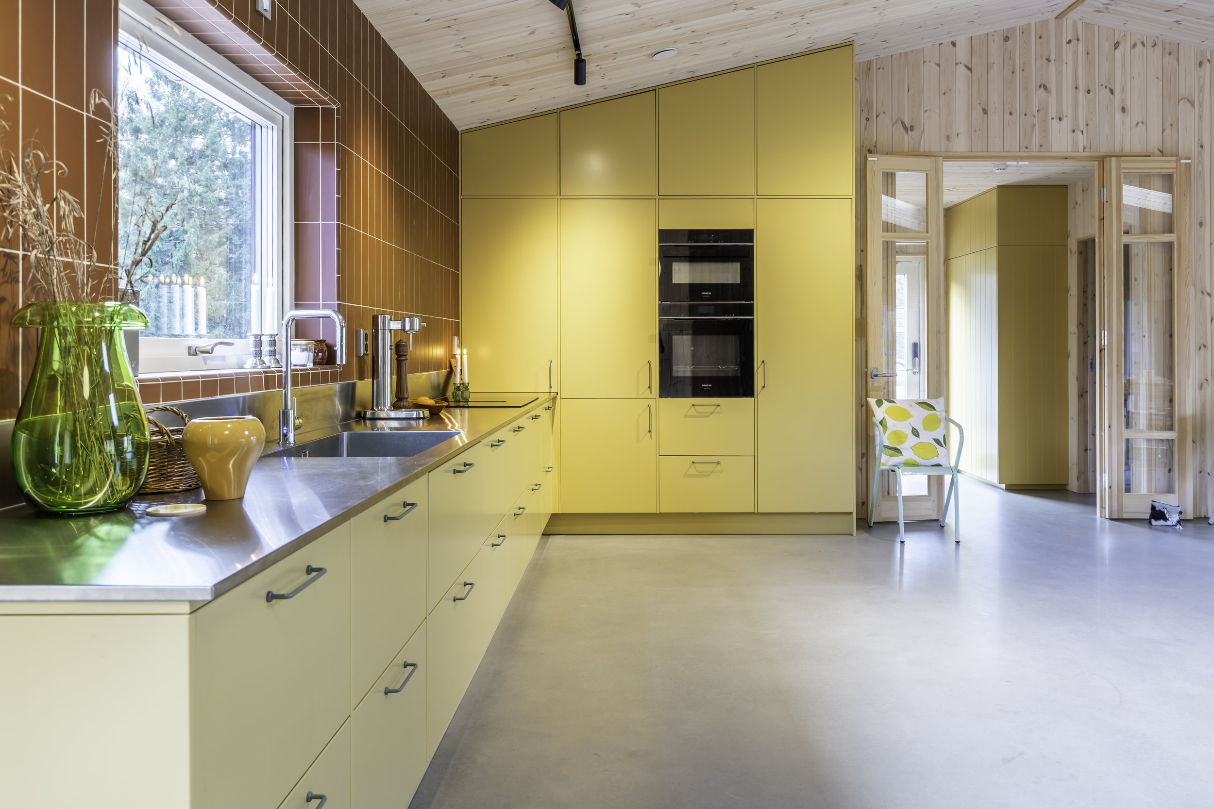 Modernt gult designkök från Smedstorps Snickeri med rostfärgat kakel och rostfri bänkskiva.