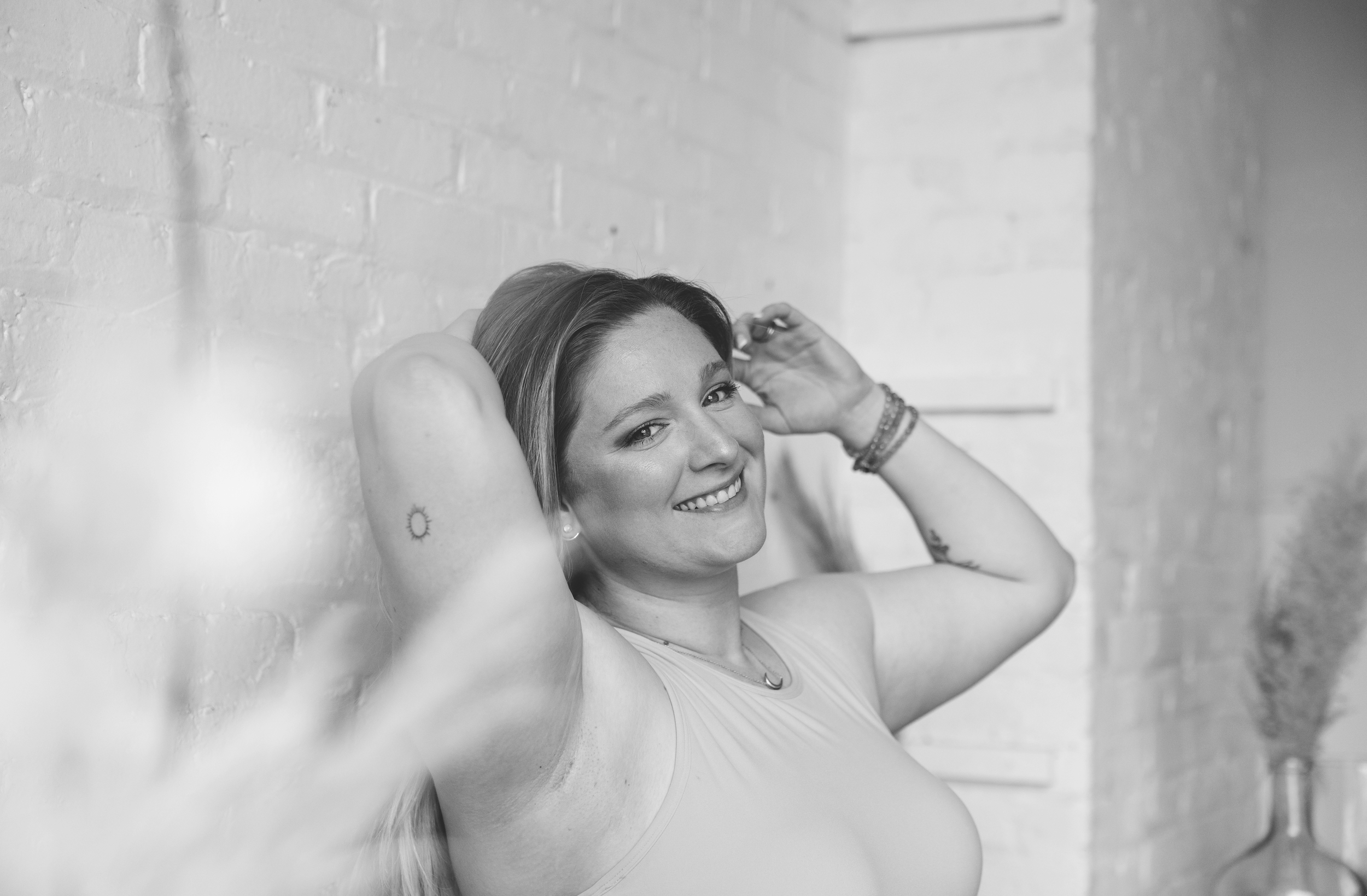 Group of women practicing yoga in a studio, standing with arms raised overhead, visible from the back, in black and white.