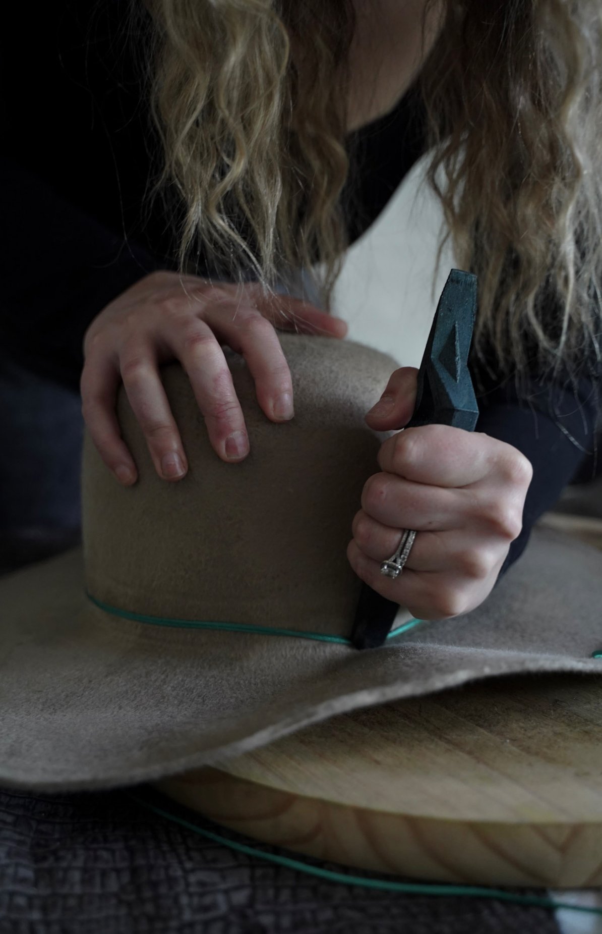 A person shaping a piece of leather with a tool, likely a leatherworking process, with focus on their hands and the leather.