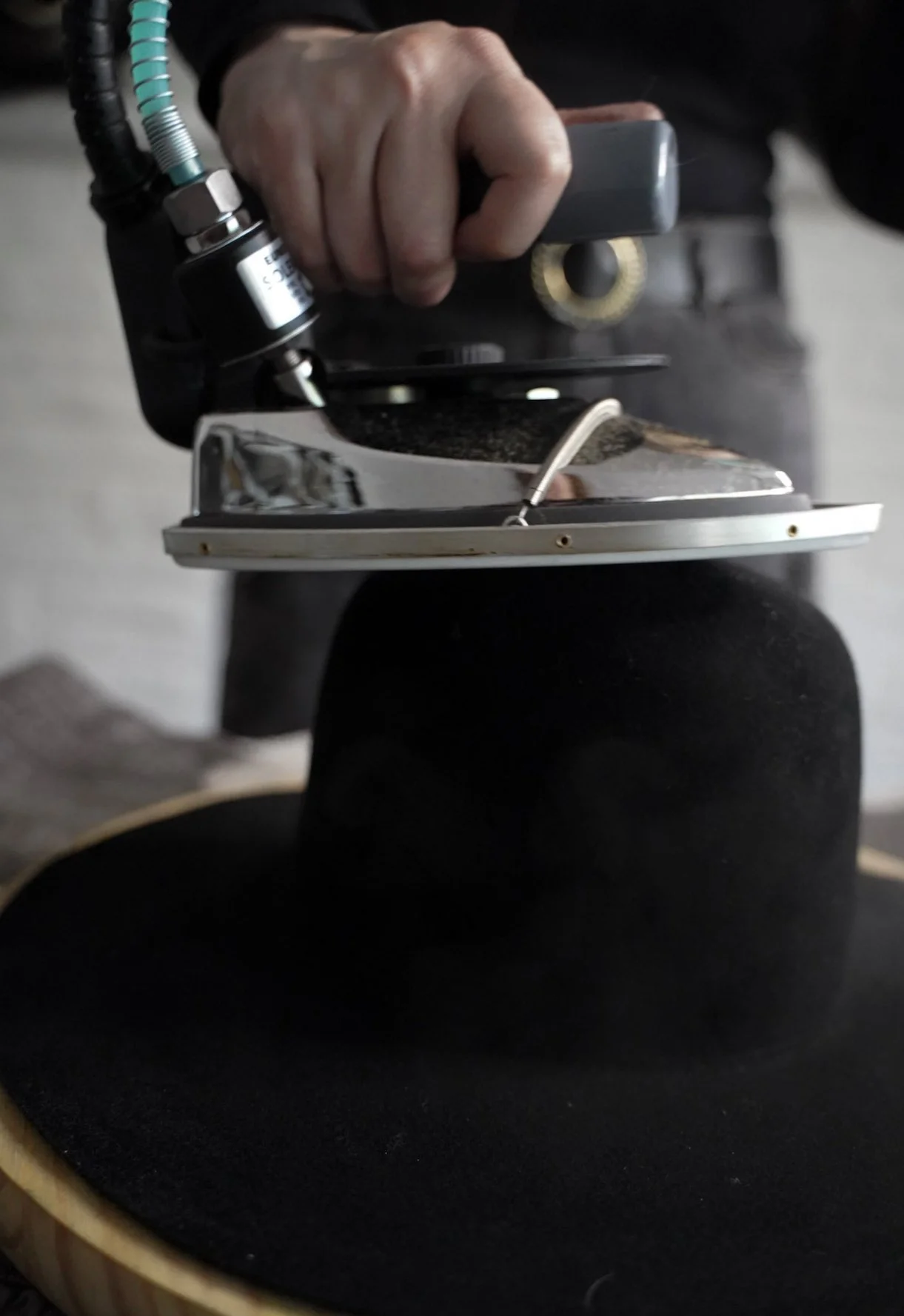 A person is ironing a black hat with a steam iron.